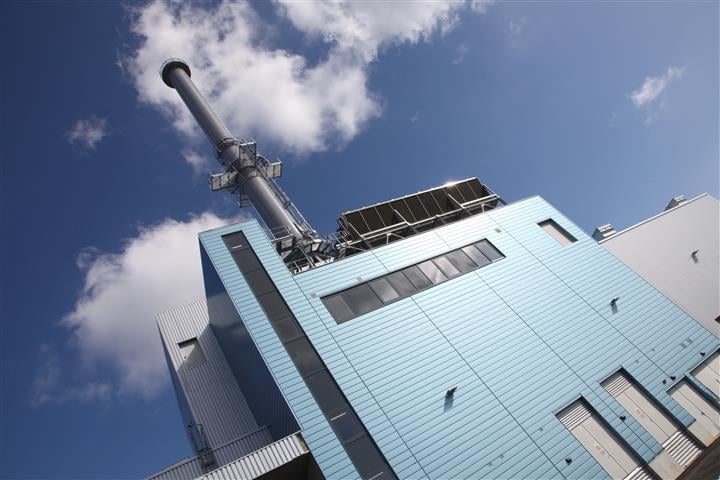A view from below of a CHP plant, framed against a clear blue sky dotted with white fluffy clouds.