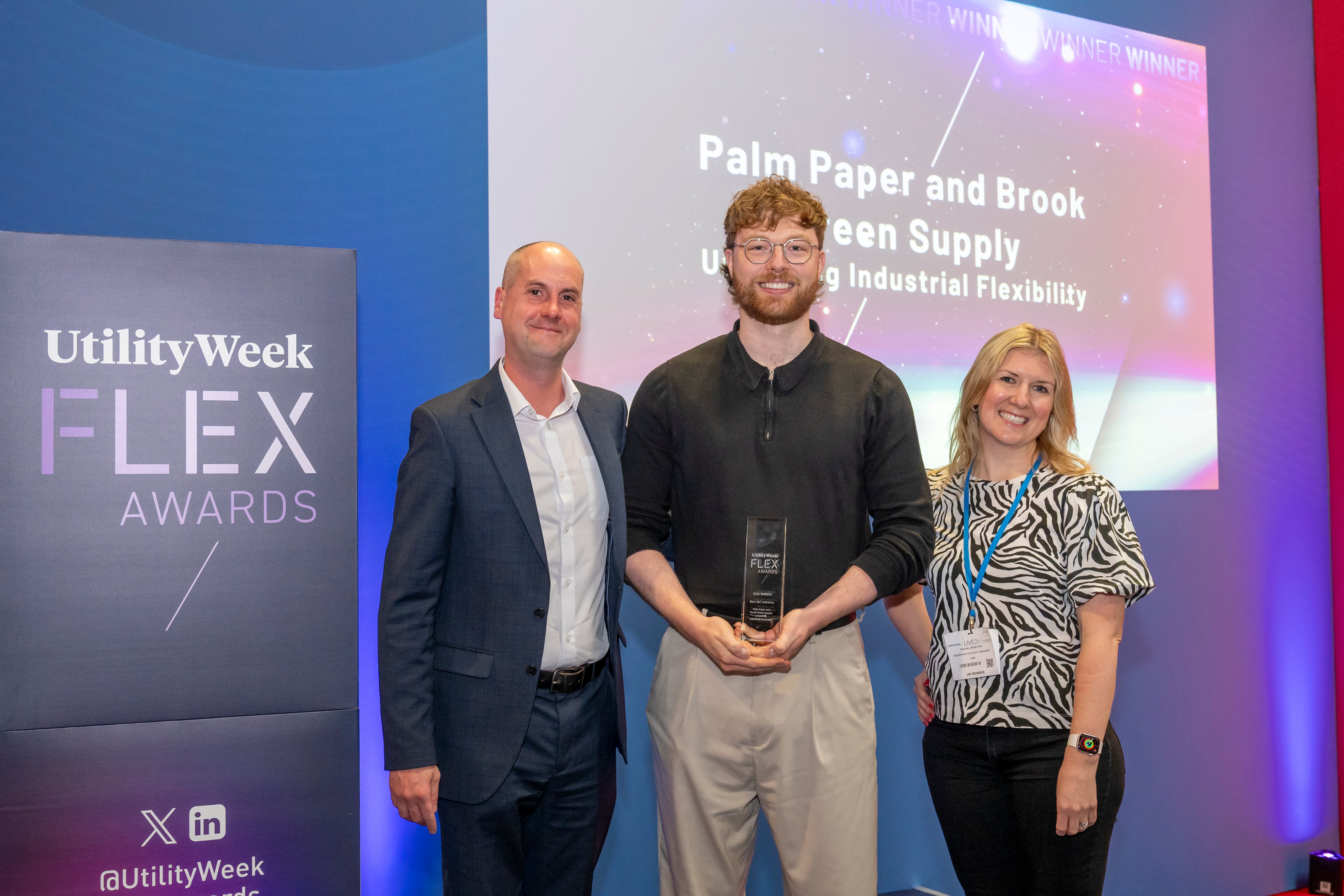 Three people stand against an awards backdrop, with the middle person holding the Utility Week Flex Award for Best I&C Initiative.
