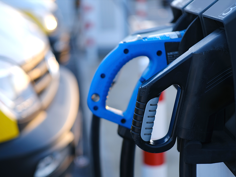 Close-up of electric vehicle charging connectors with parked vehicles blurred in the background.
