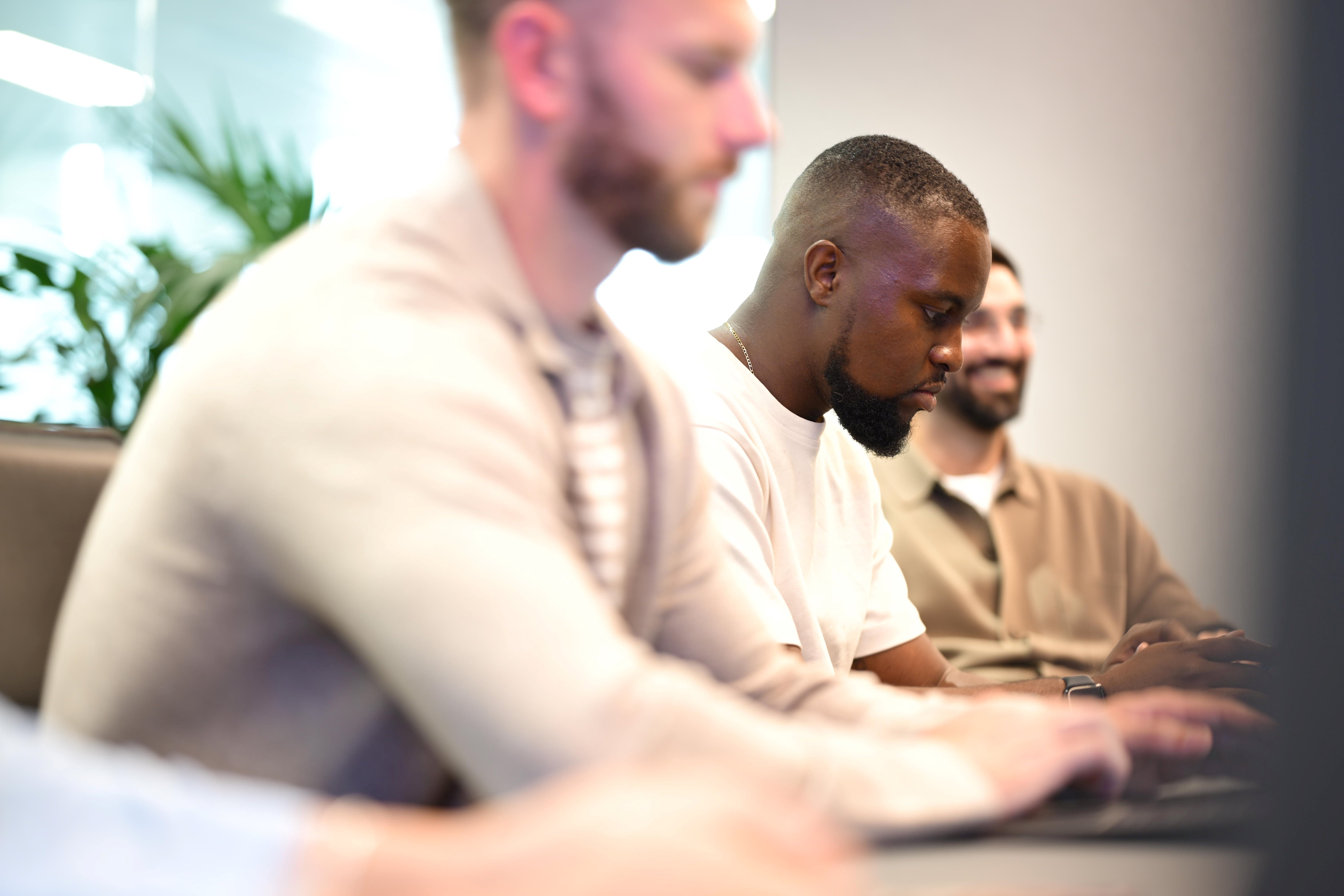 A side view of three people sat in a row on laptops.