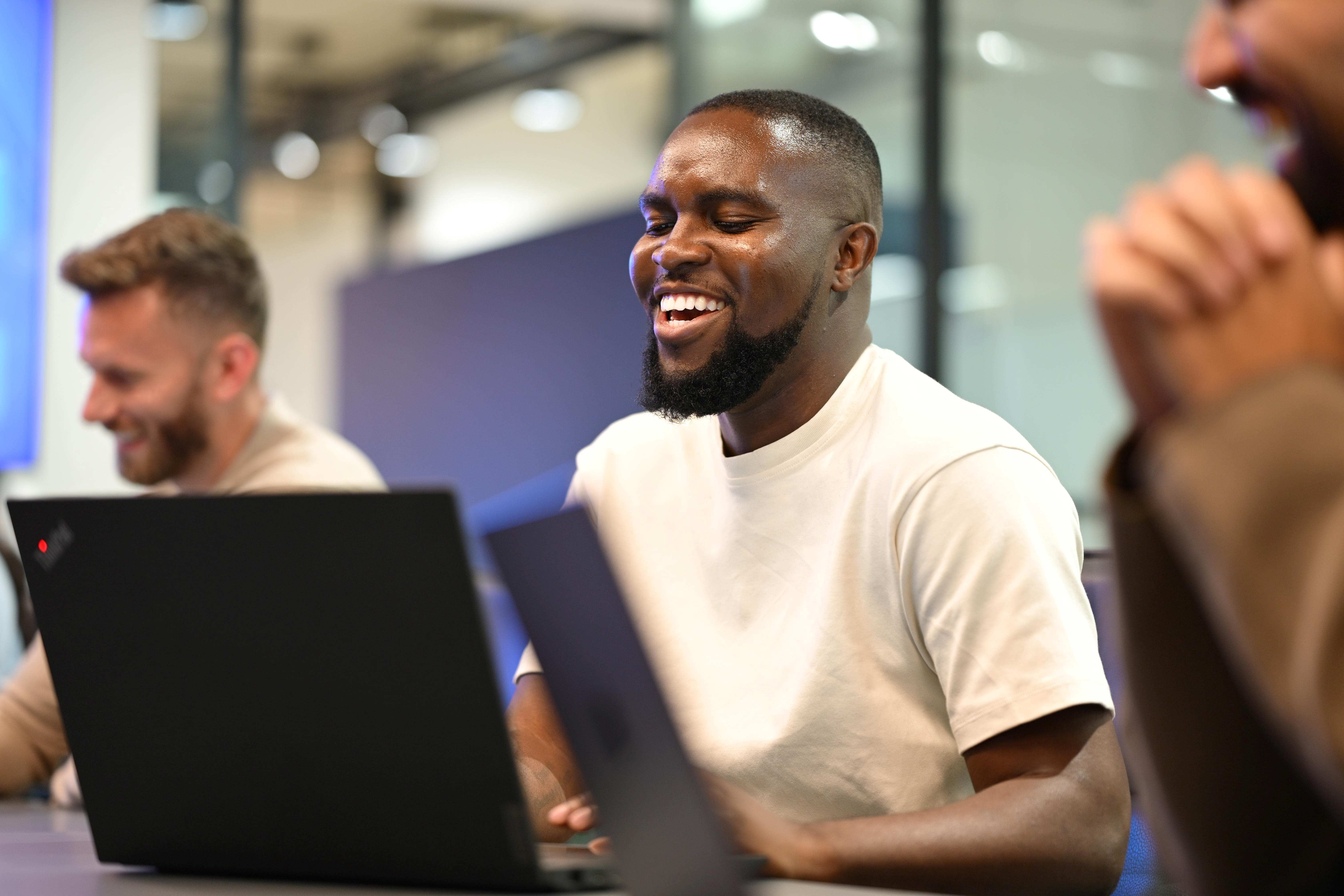 Person laughing looking at a laptop, amongst other people.