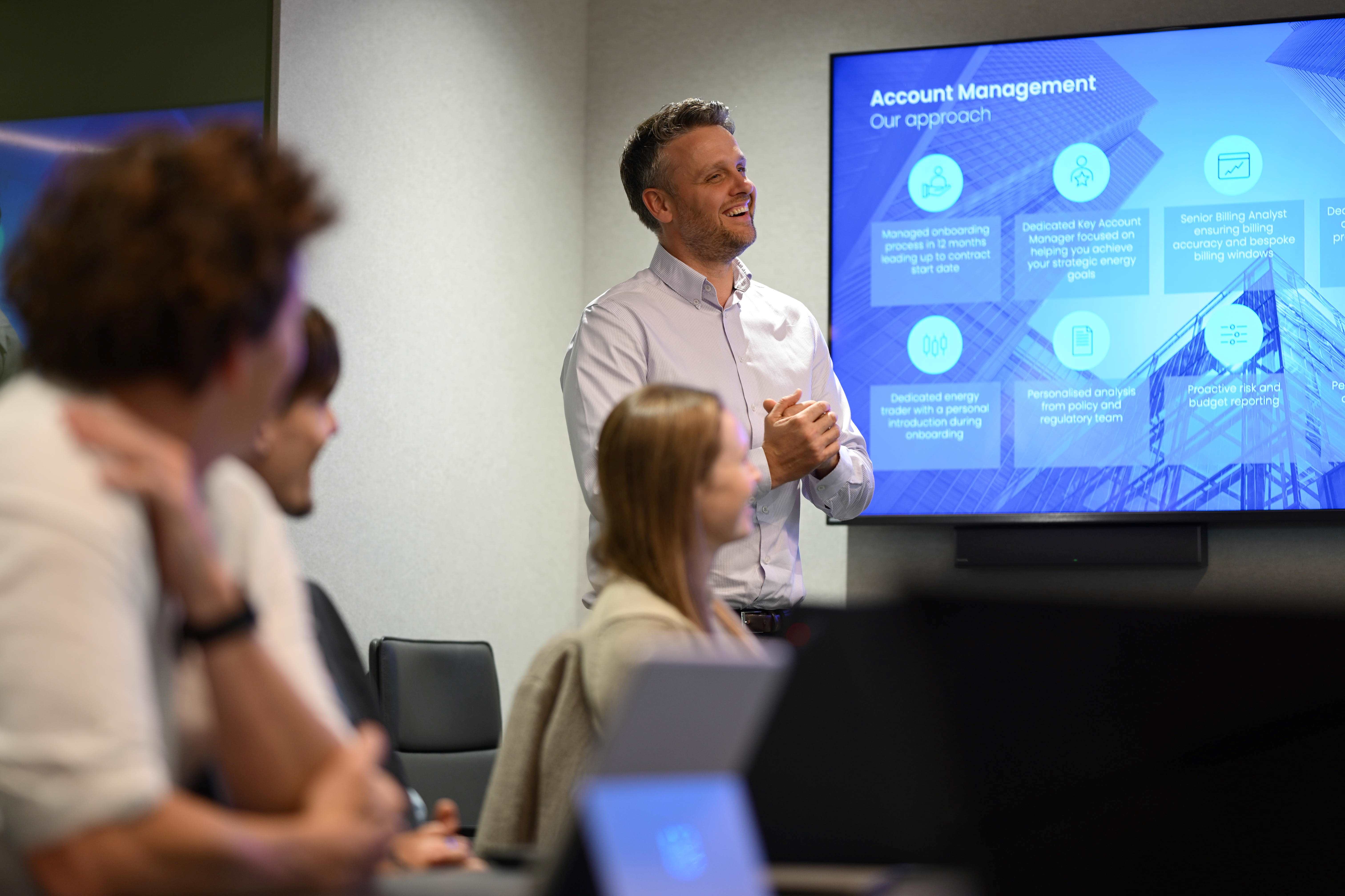 A person smiles during a work presentation as people look on.