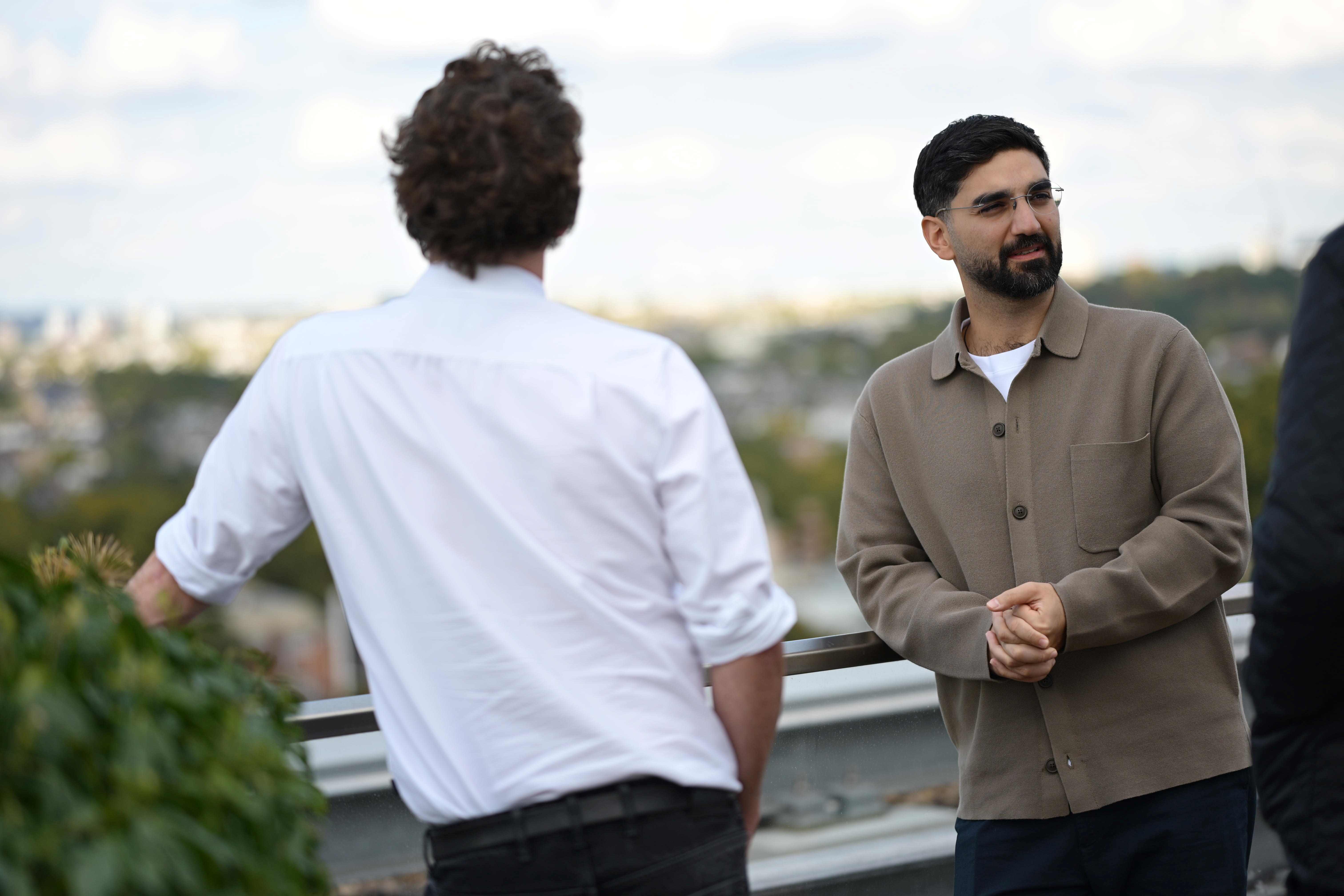 People talk in a rooftop garden with a city skyline.