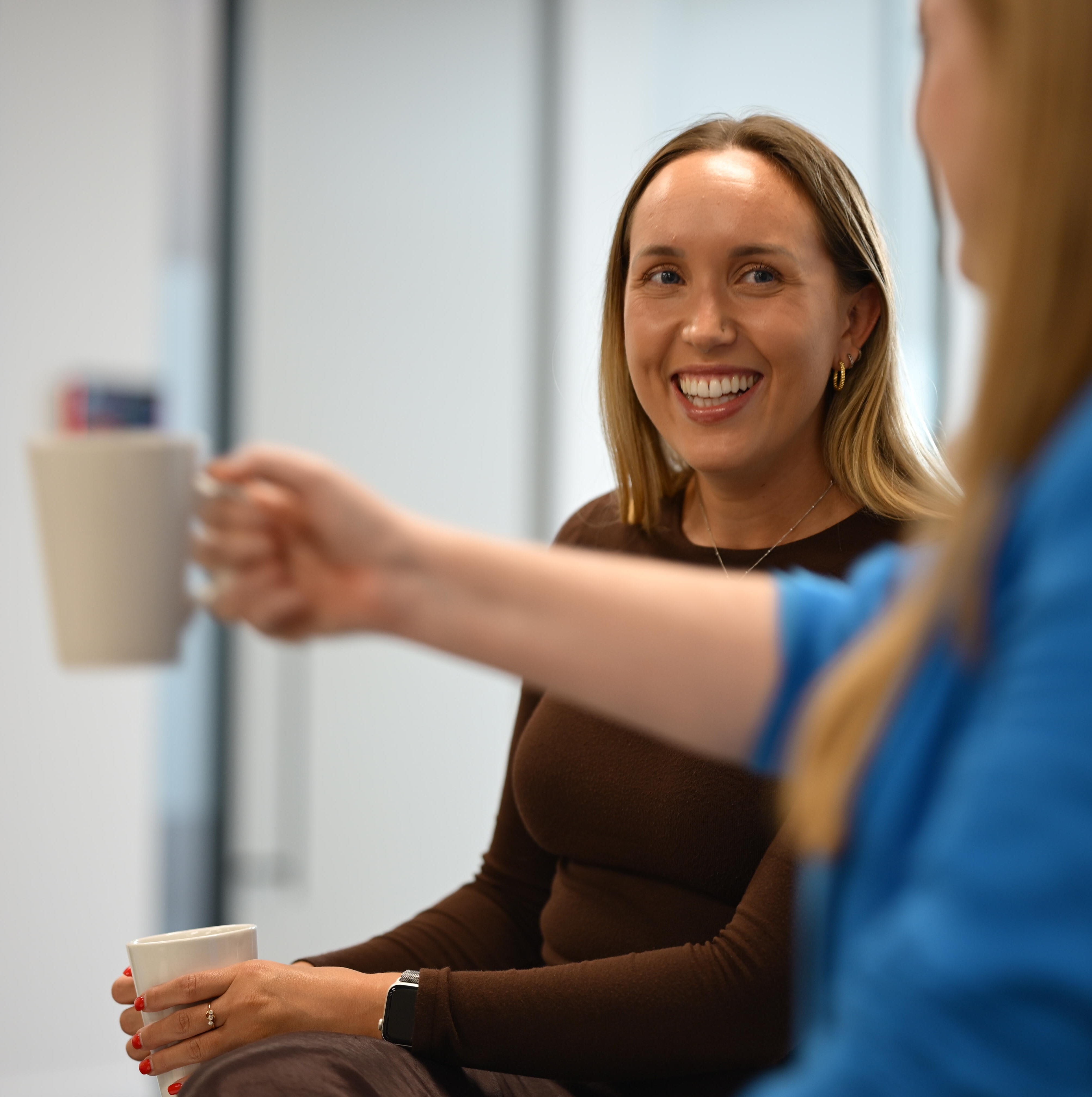 Two people sat together smiling and drinking from mugs.