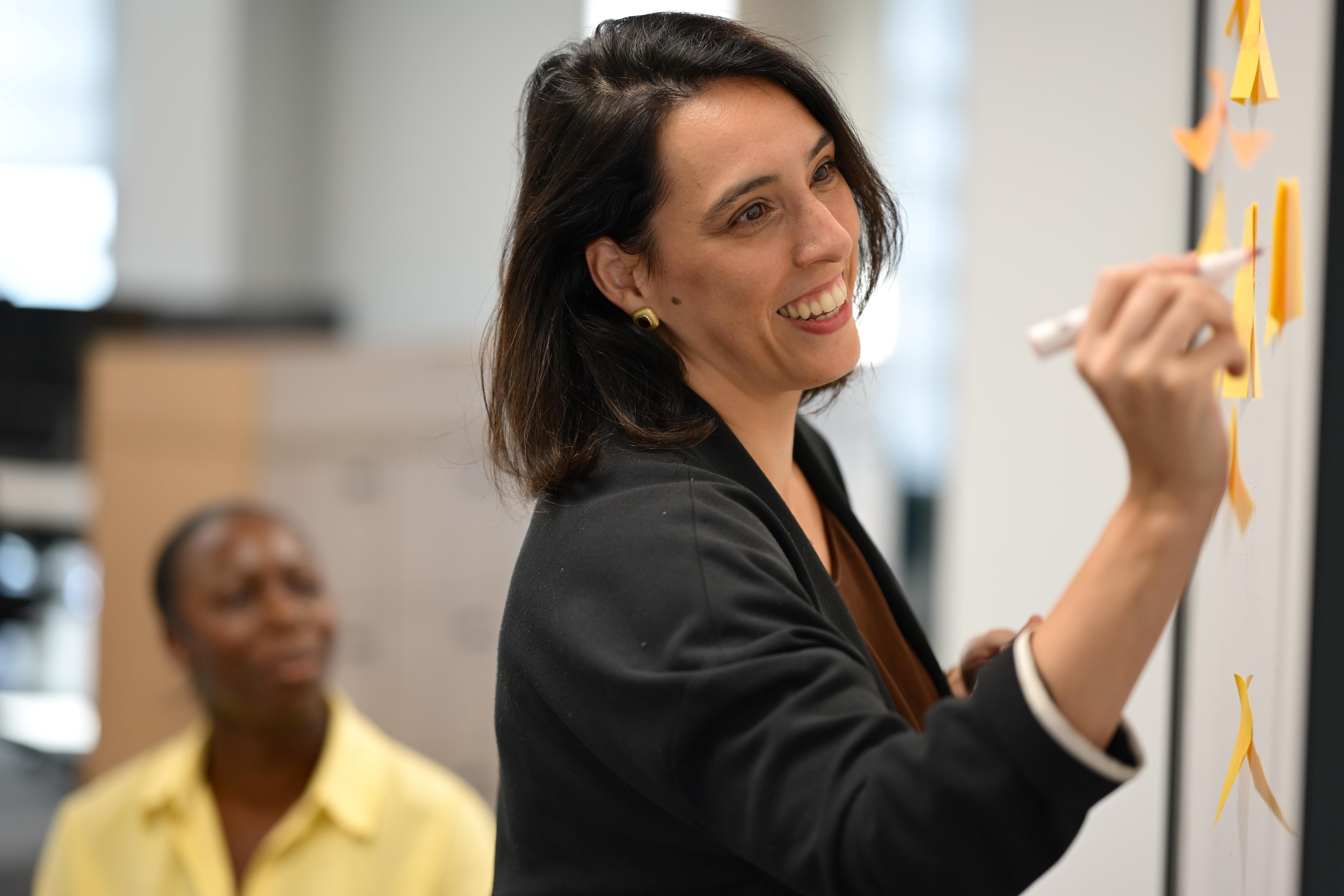 Person smiling and writing on whiteboard.