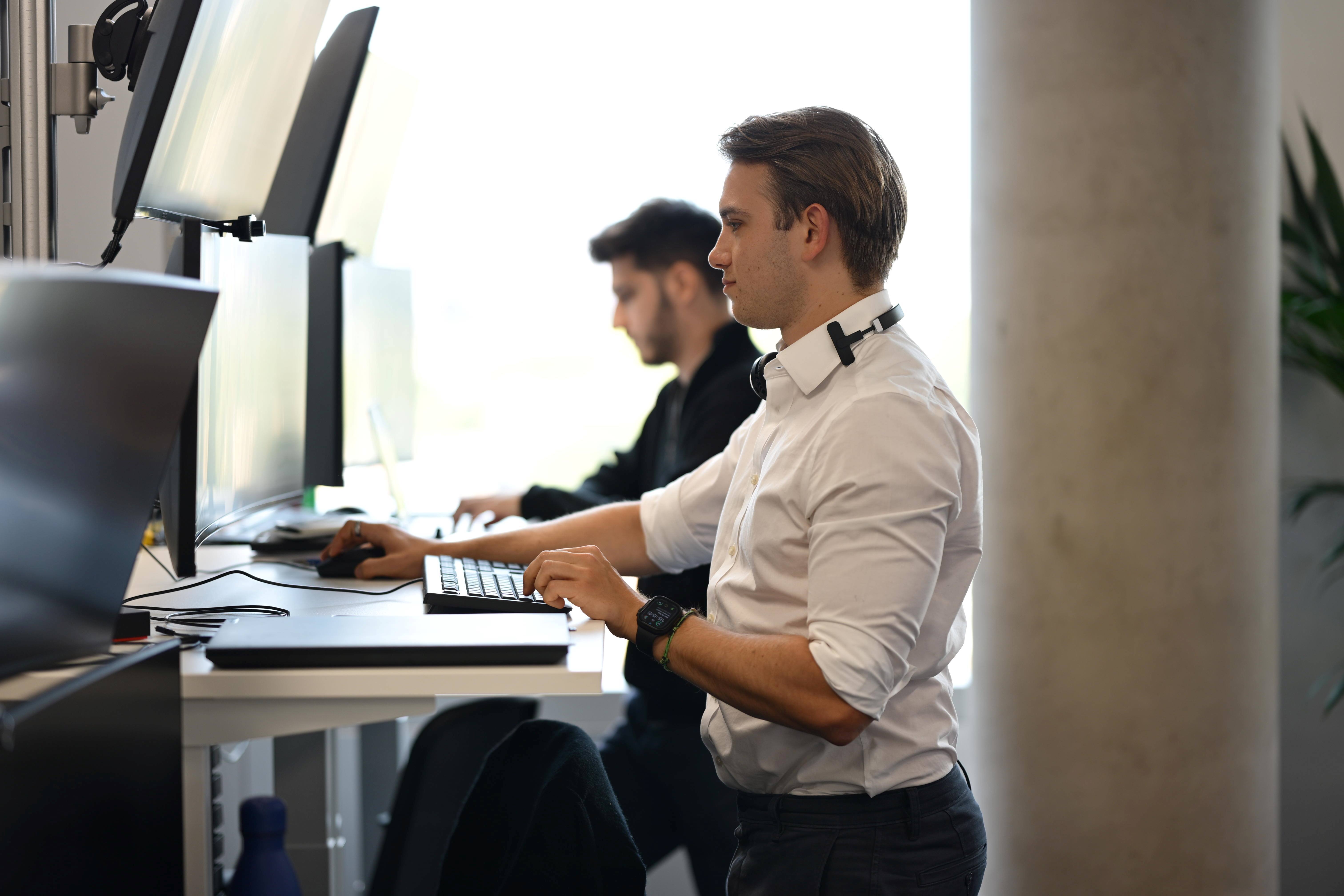 A side view of two people standing and looking at screens.