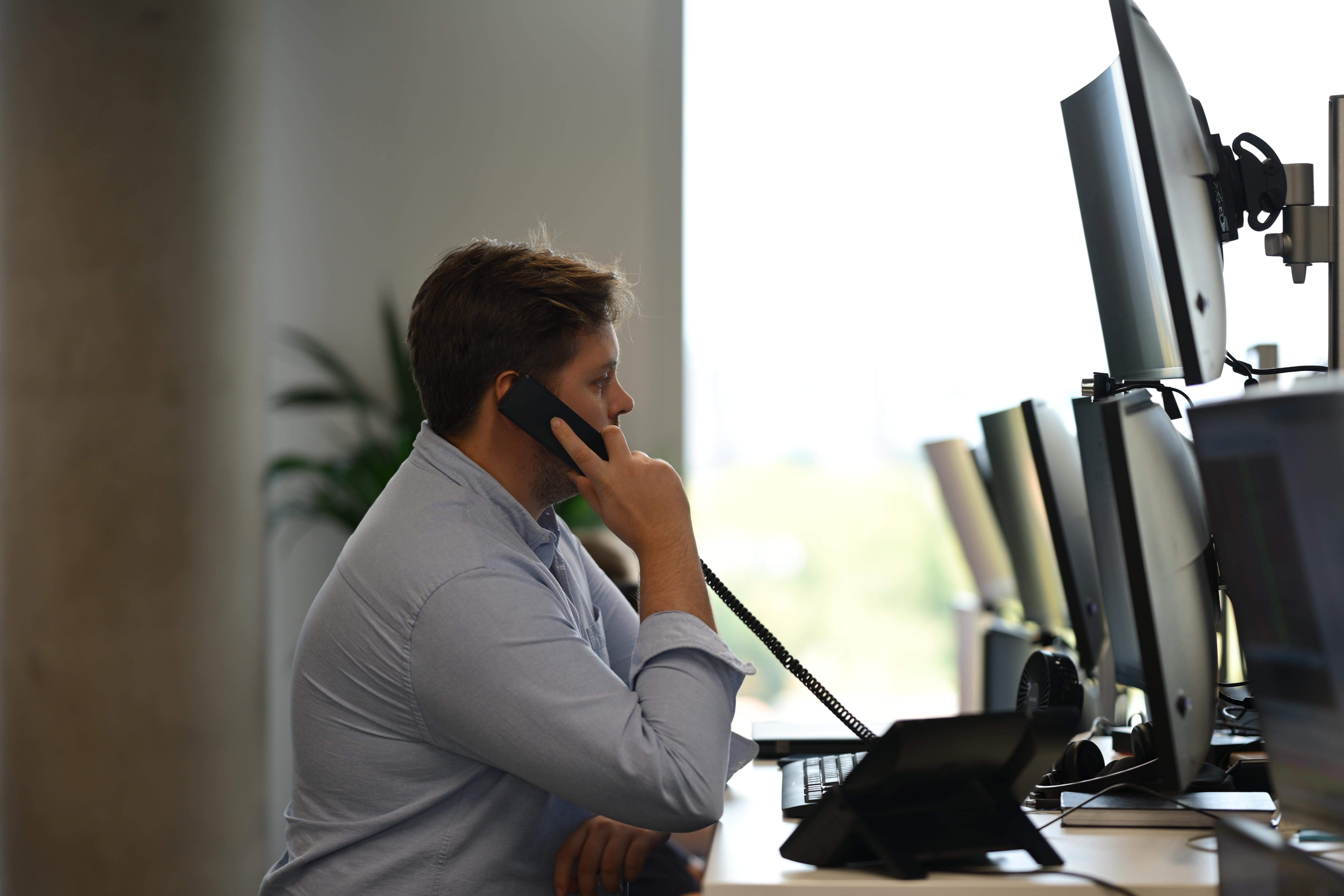 A person sat in front of a screen makes a phone call.