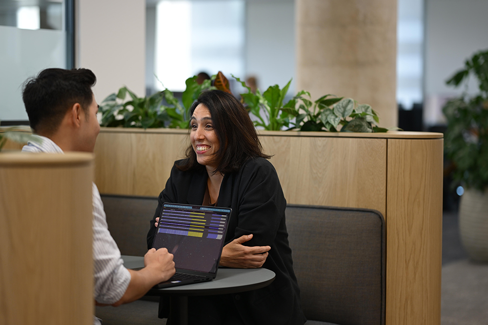 Two people talk and smile looking at a laptop.