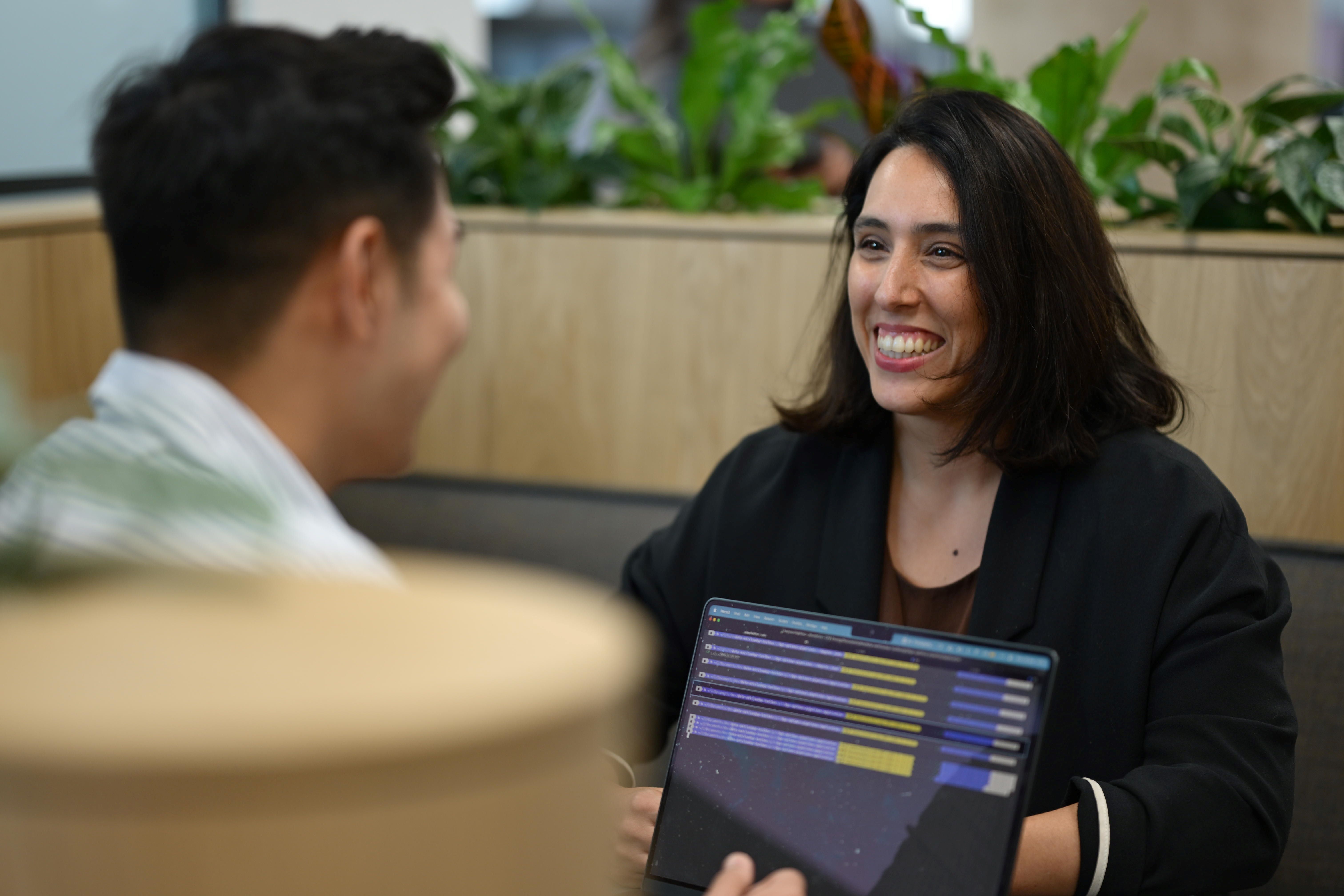 Two people talk and smile looking at a laptop.
