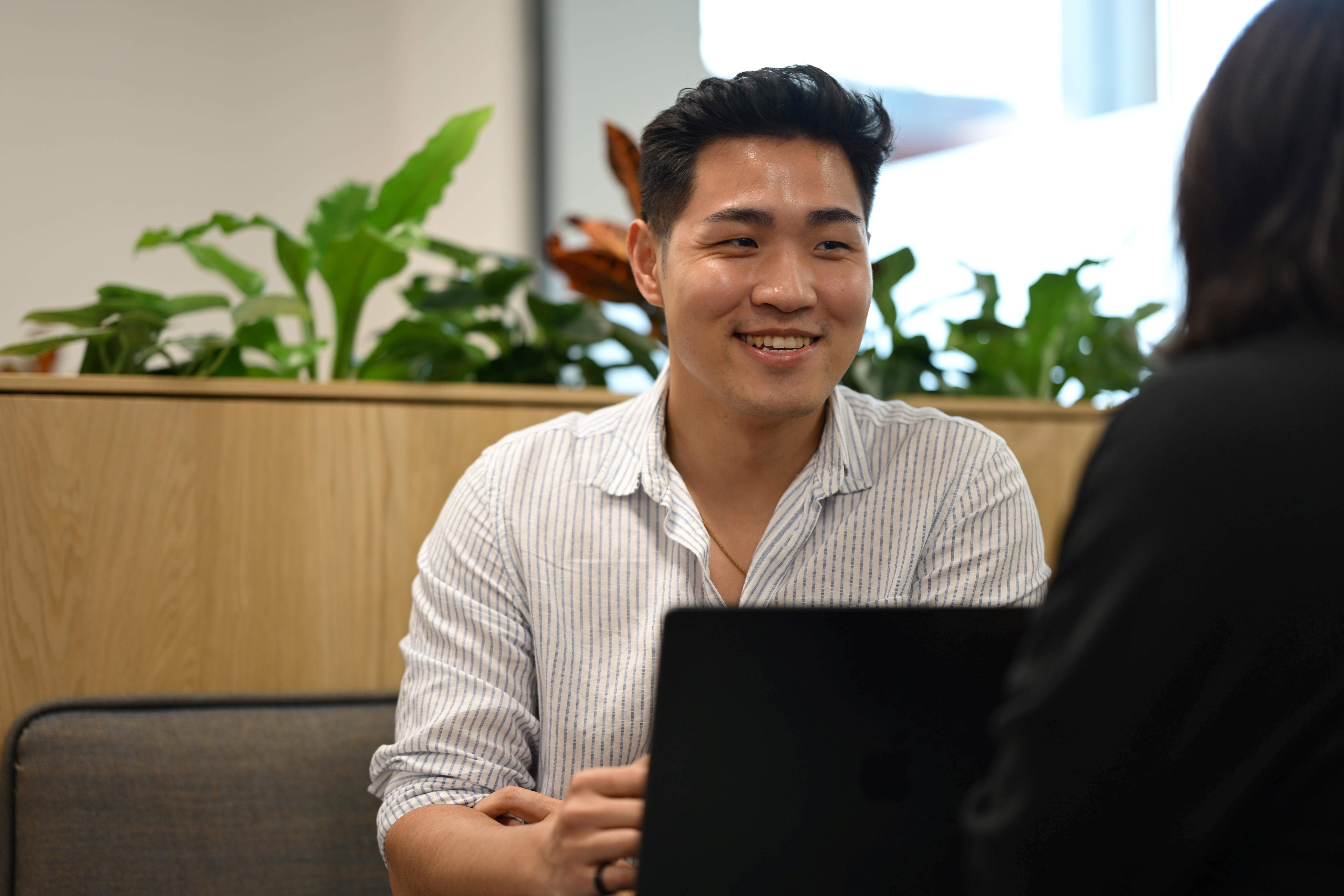A person with a laptop smiles as they look at someone opposite them.