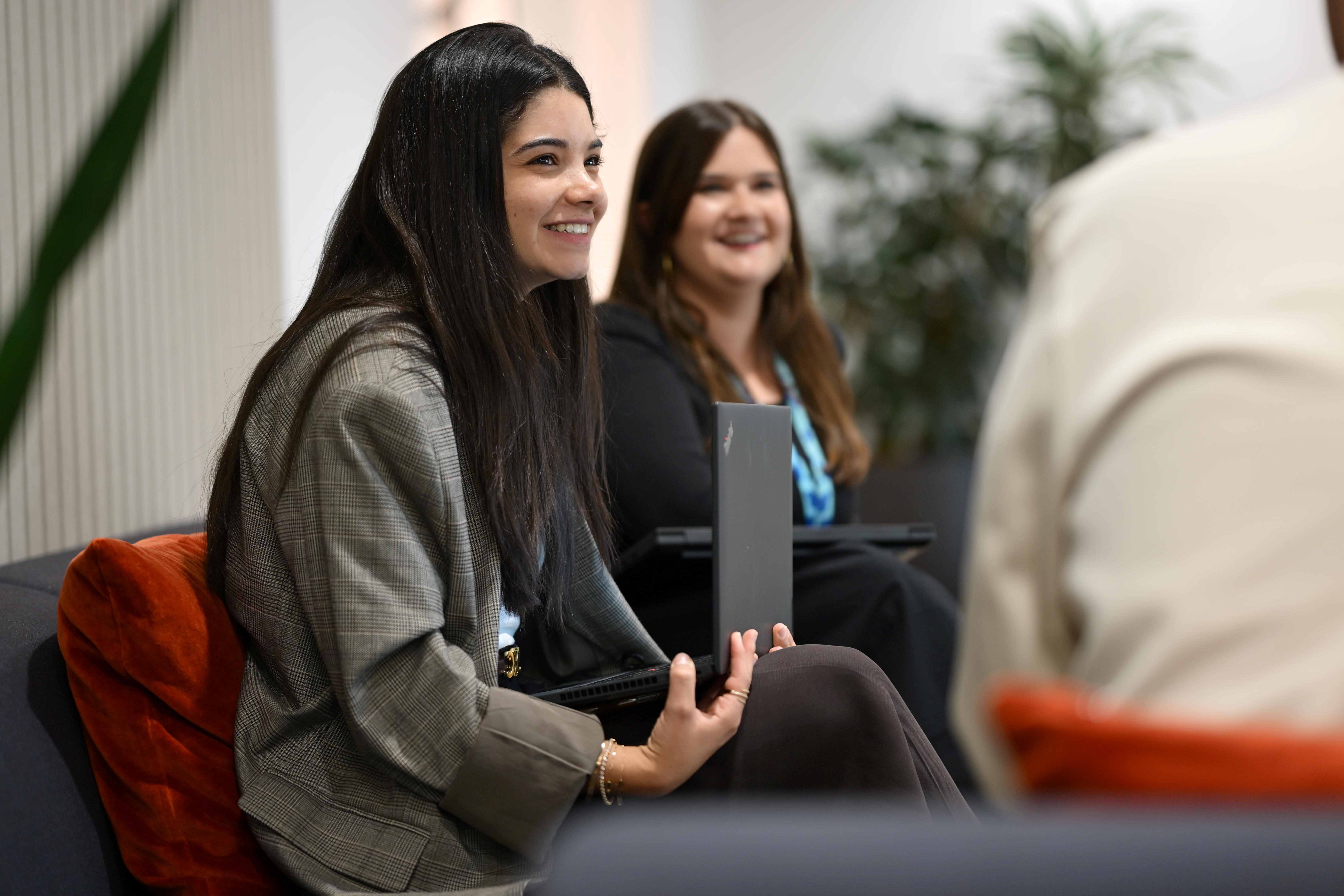 Two people sat down with laptops smile as they look at someone sat to their side.