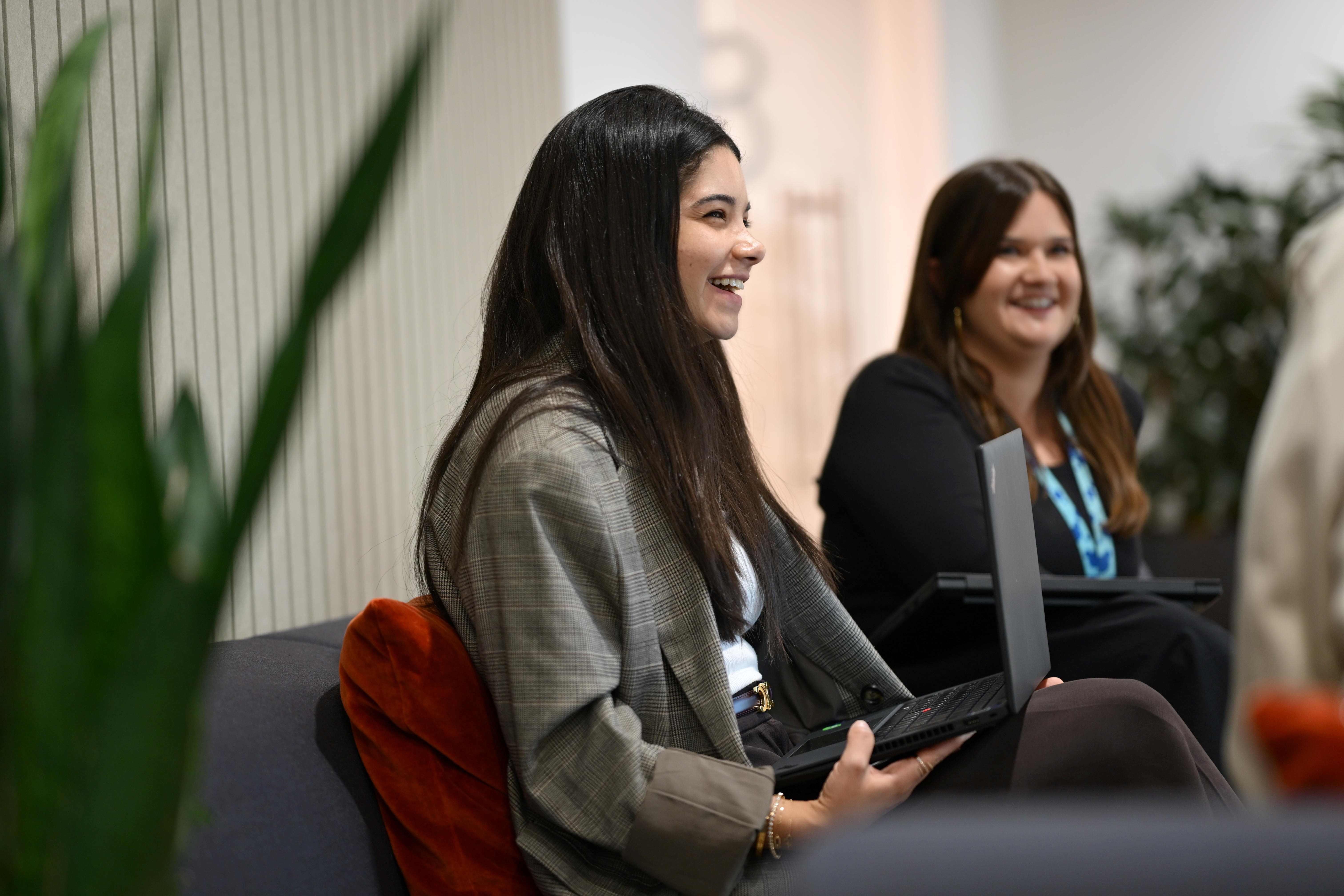 A side view of two people with laptops laughing as they look at someone opposite them.