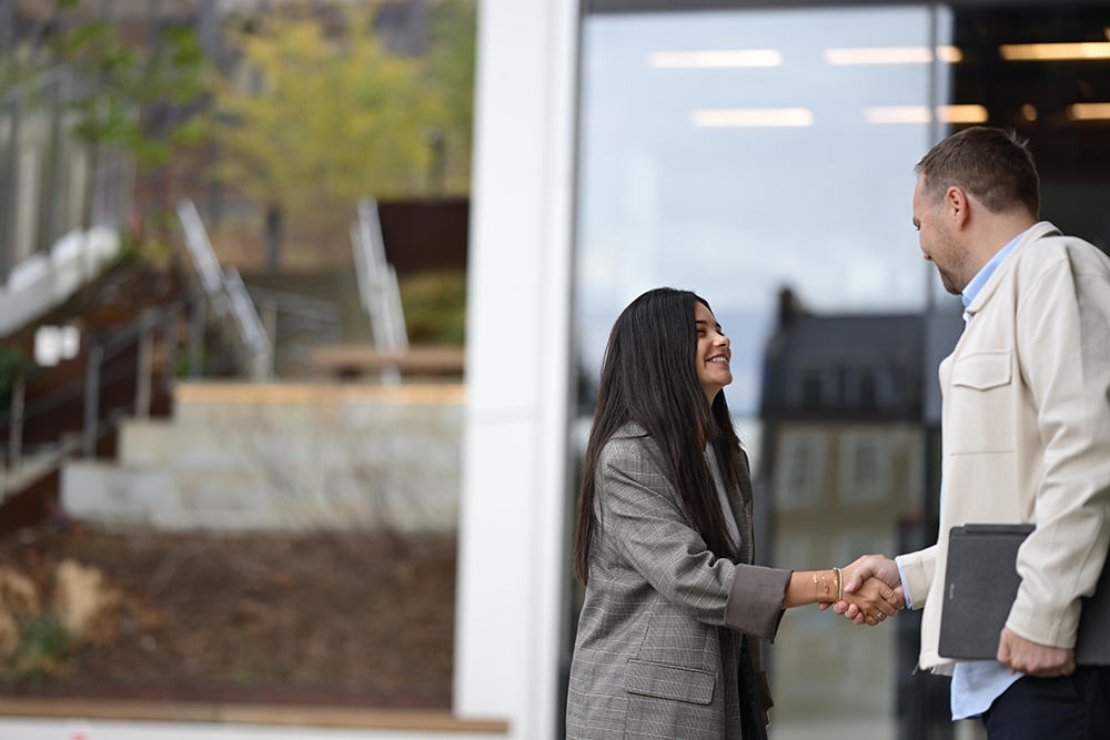 Two people shake hands outside an office building.