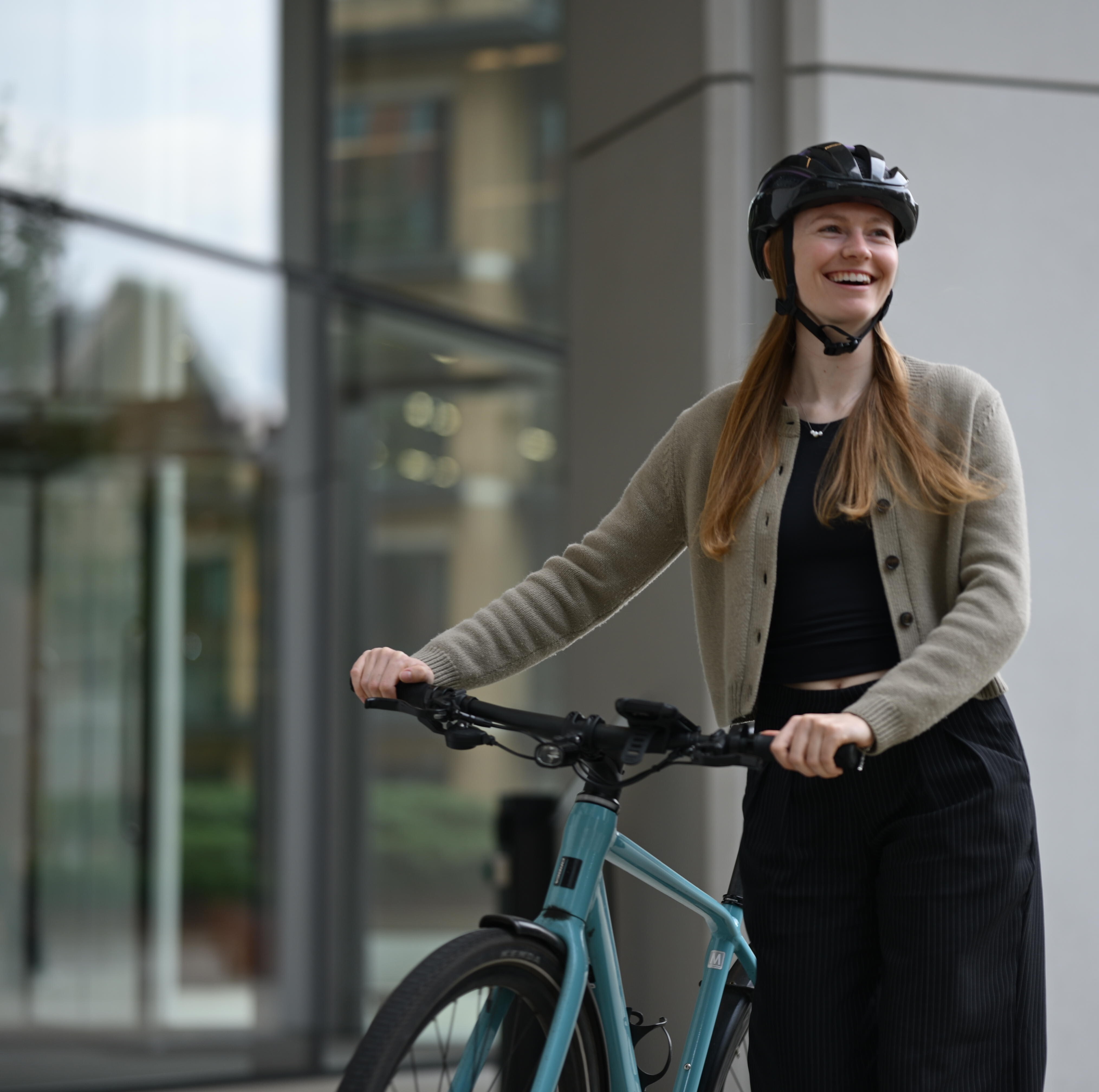 A person wheeling a bicycle smiles as they look off to the side.