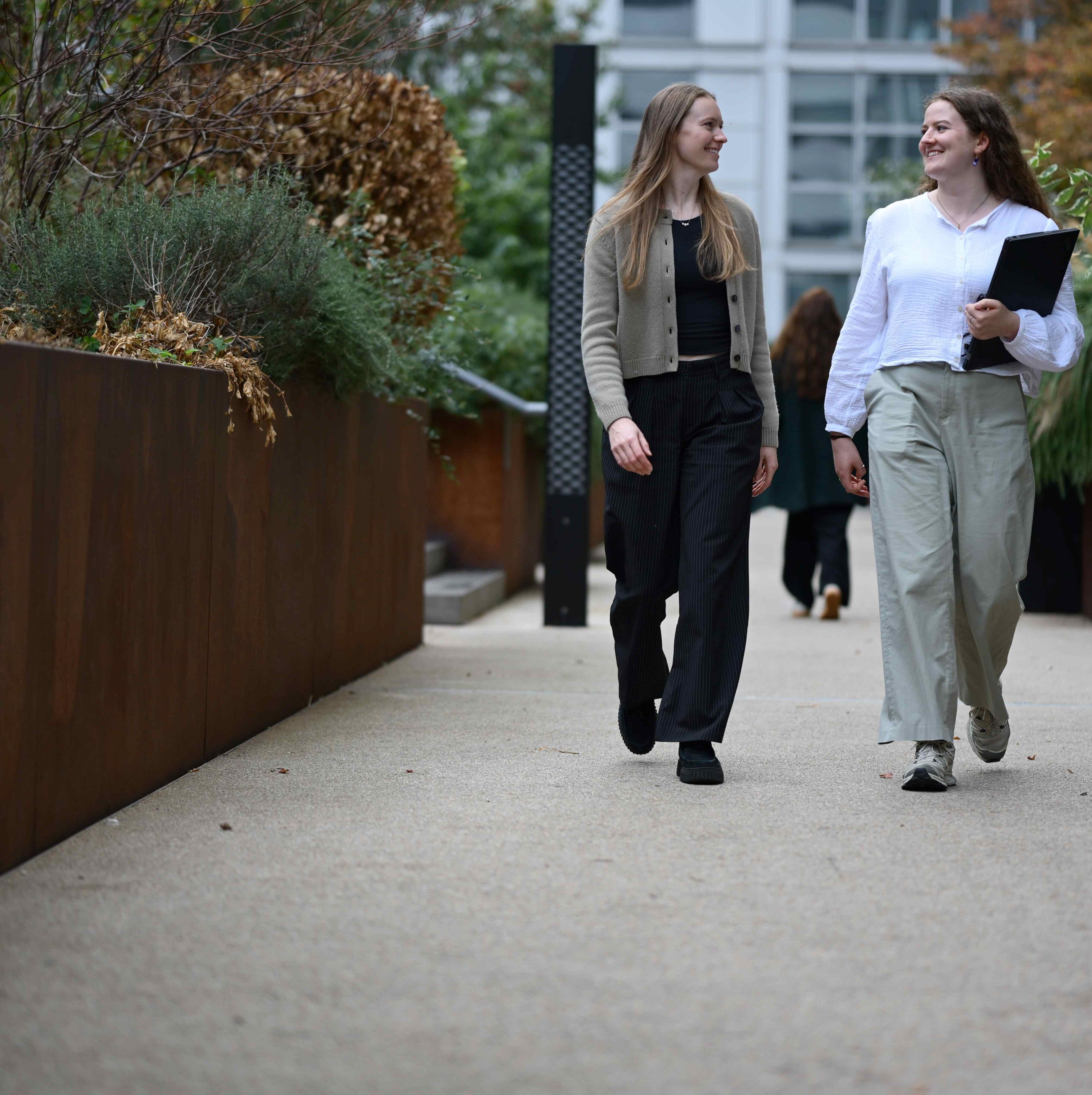Two people smile at each other as they walk through a garden.