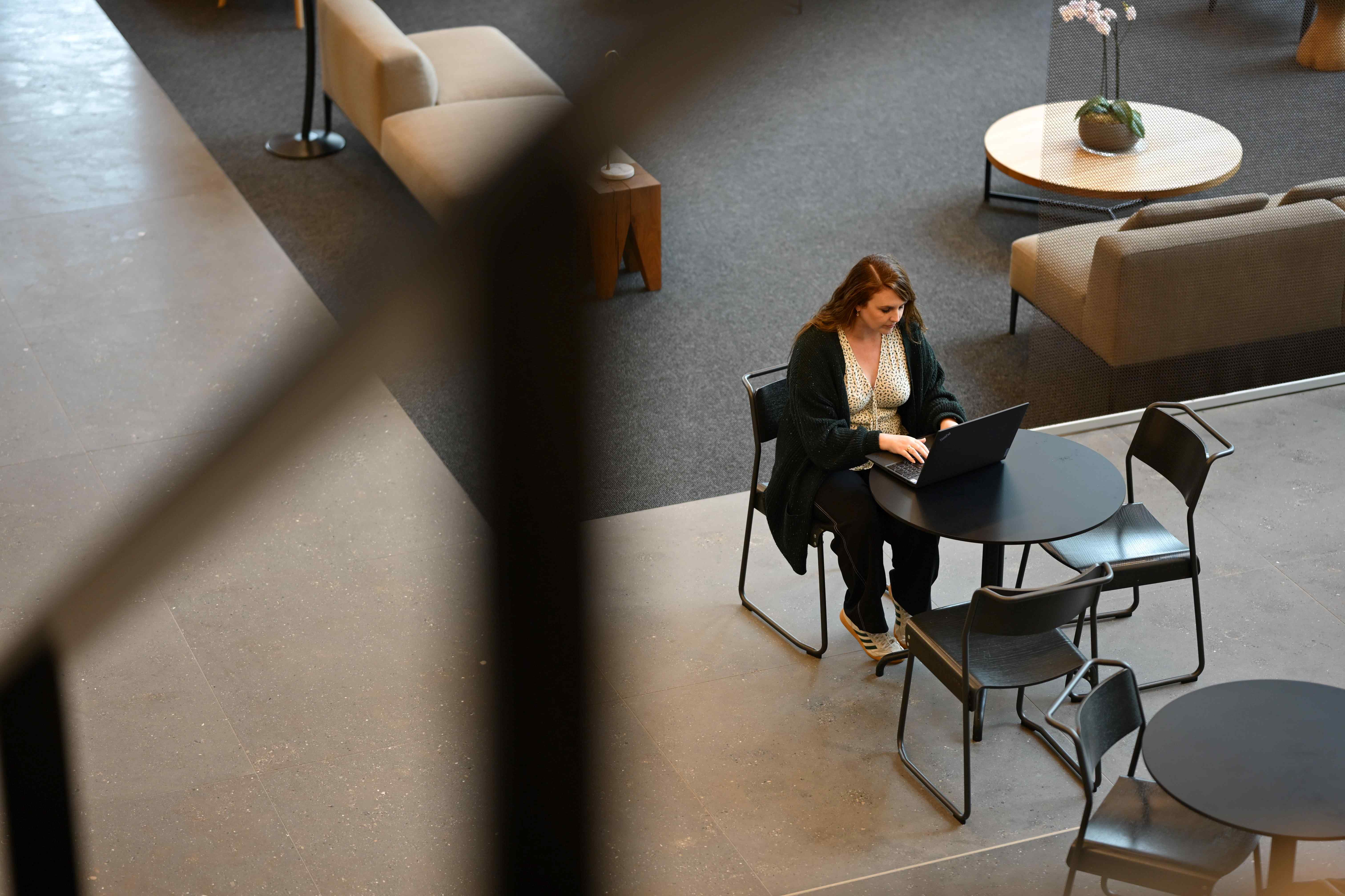 A birdseye view of a person sat at a small table with a laptop.