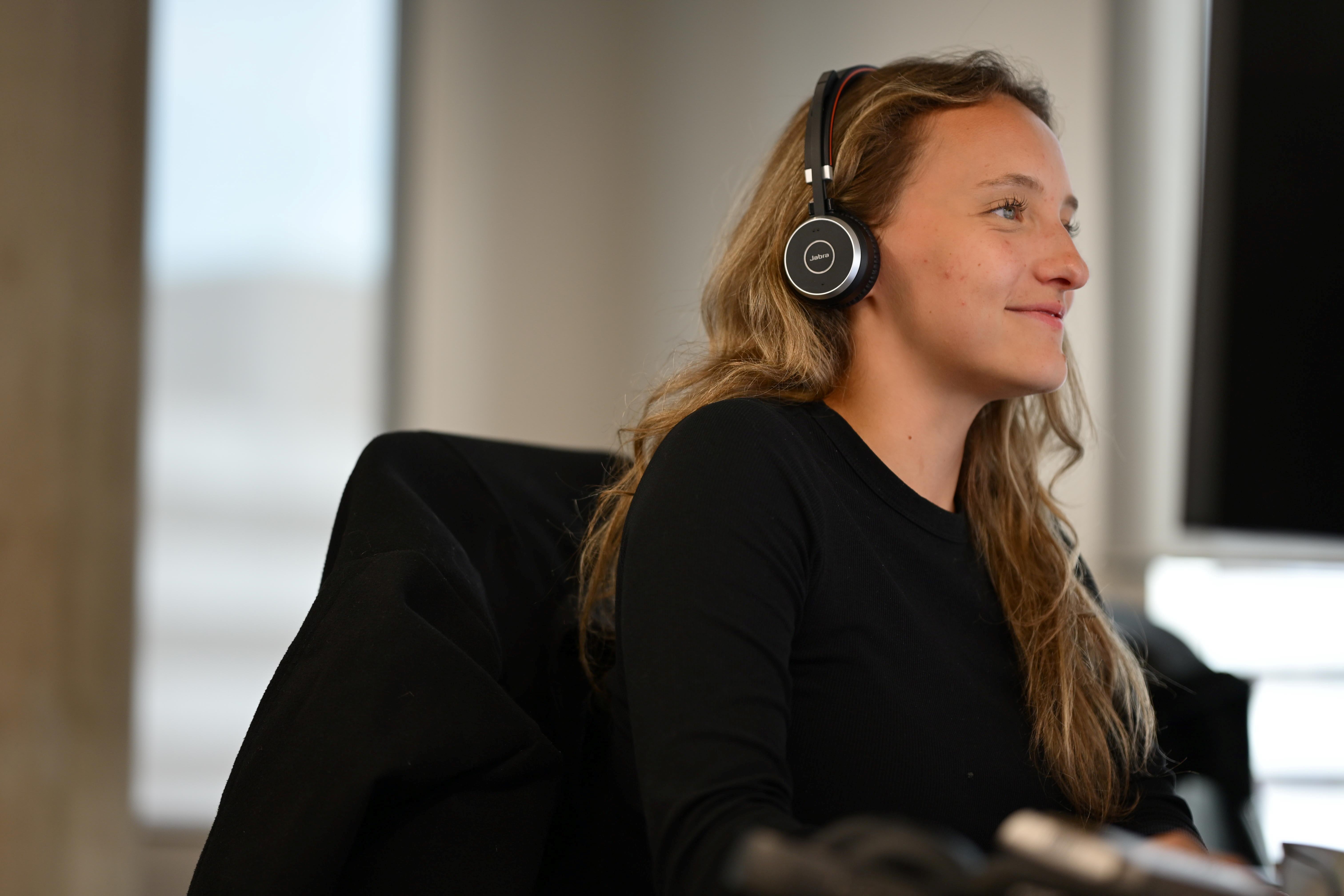 A person with a headset smiles as they look at laptop.