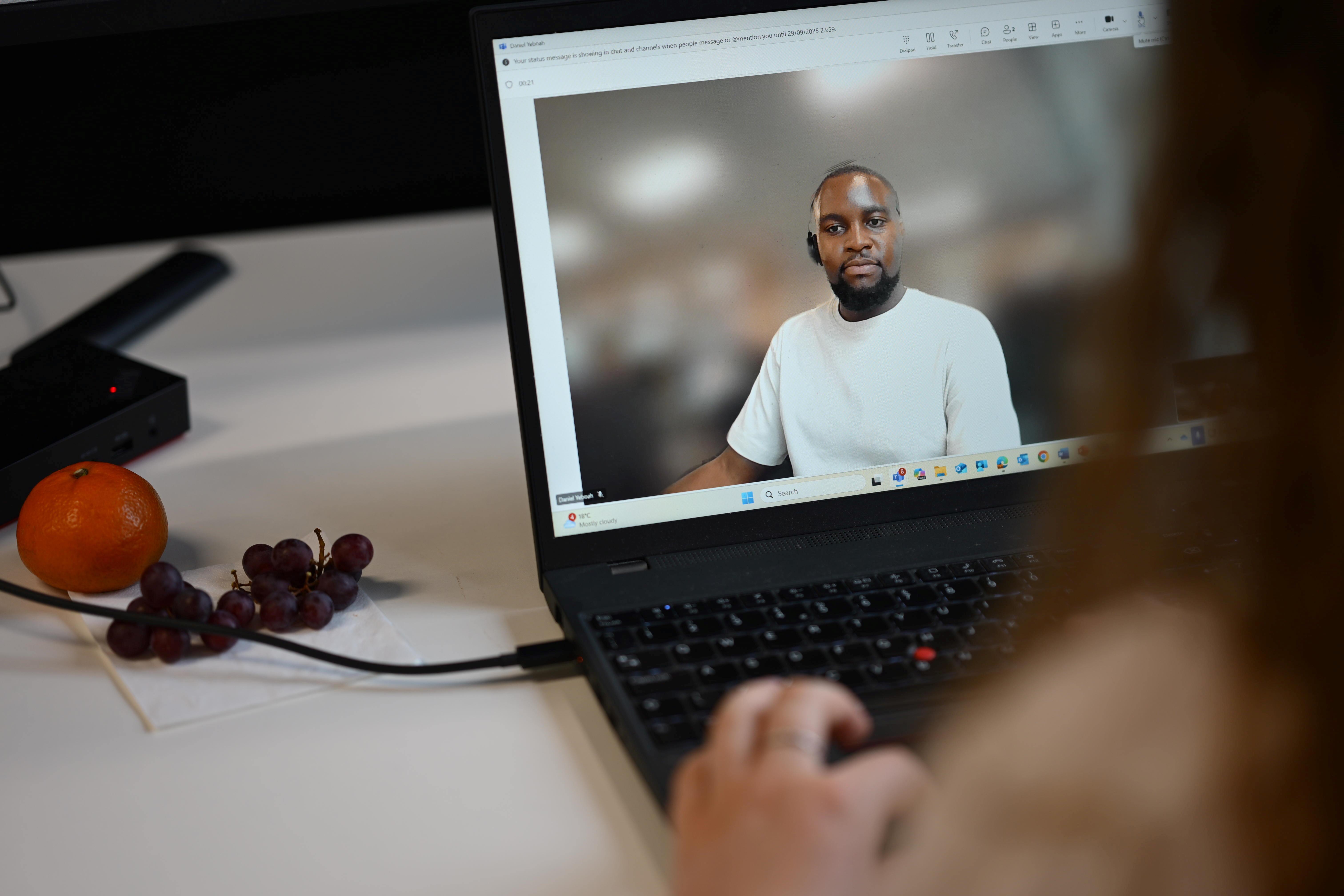 A person sat at a desk with a laptop speaks to another person over a video call.