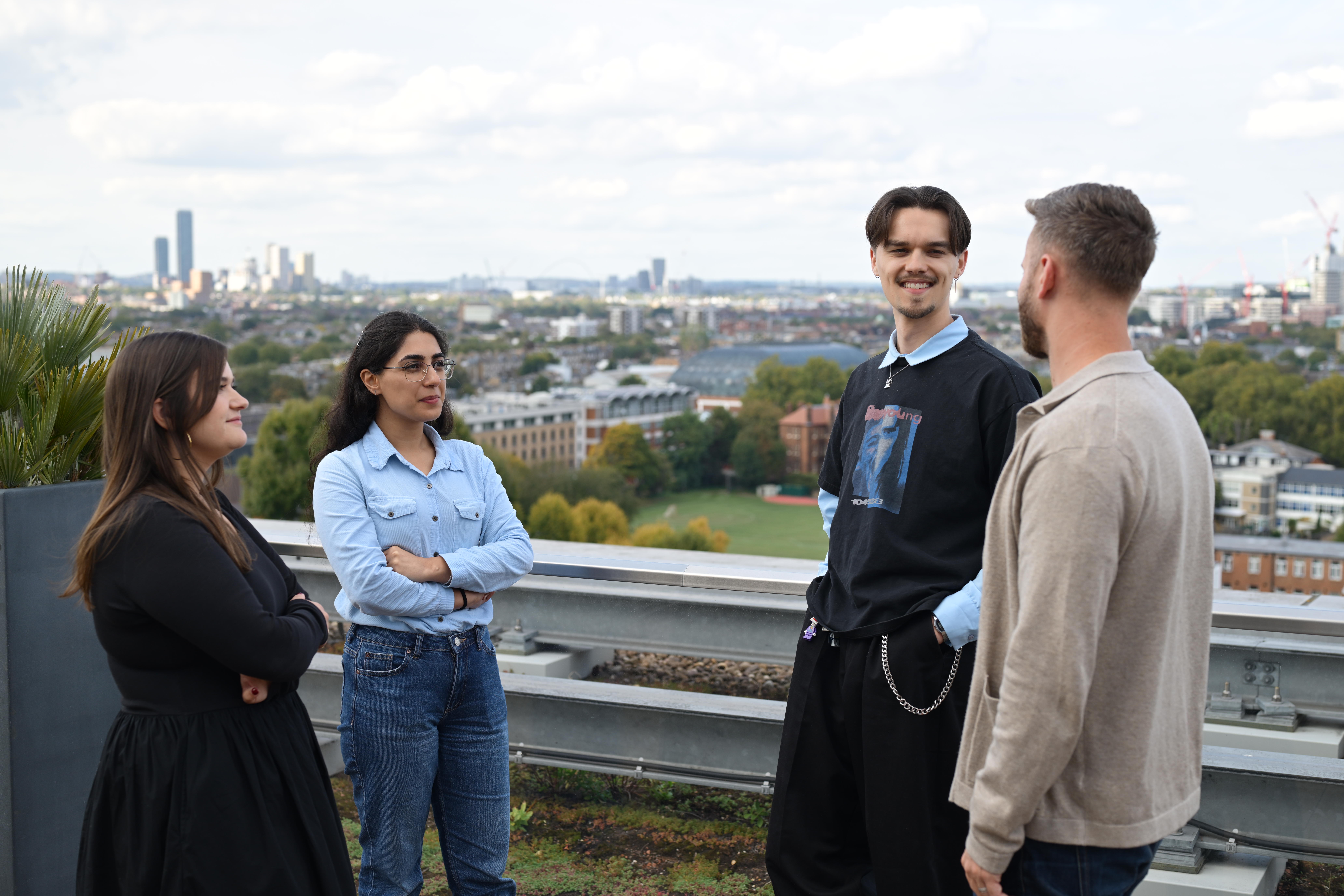 People talk in a rooftop garden with a city skyline.