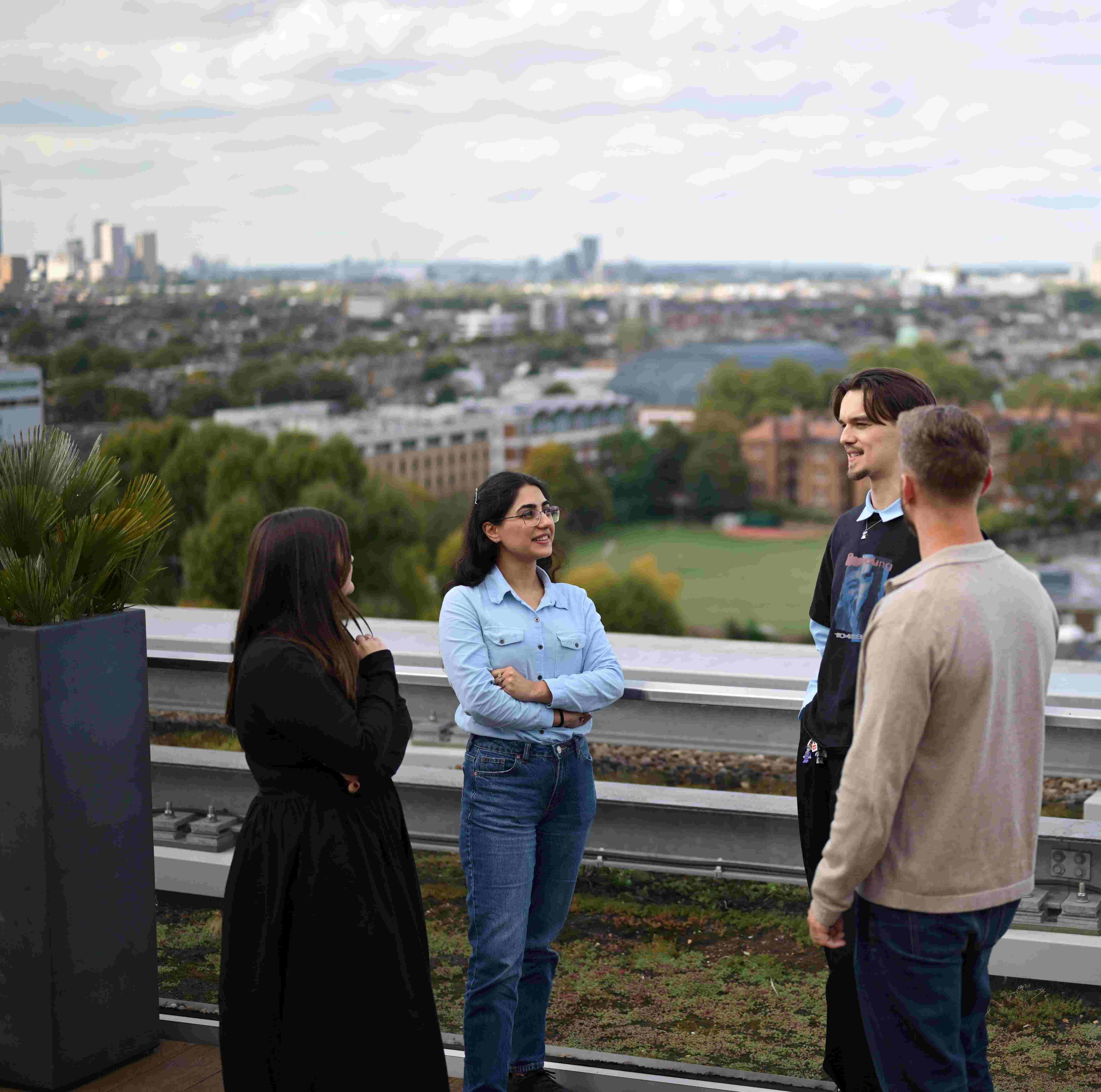 People talk in a rooftop garden with a city skyline.