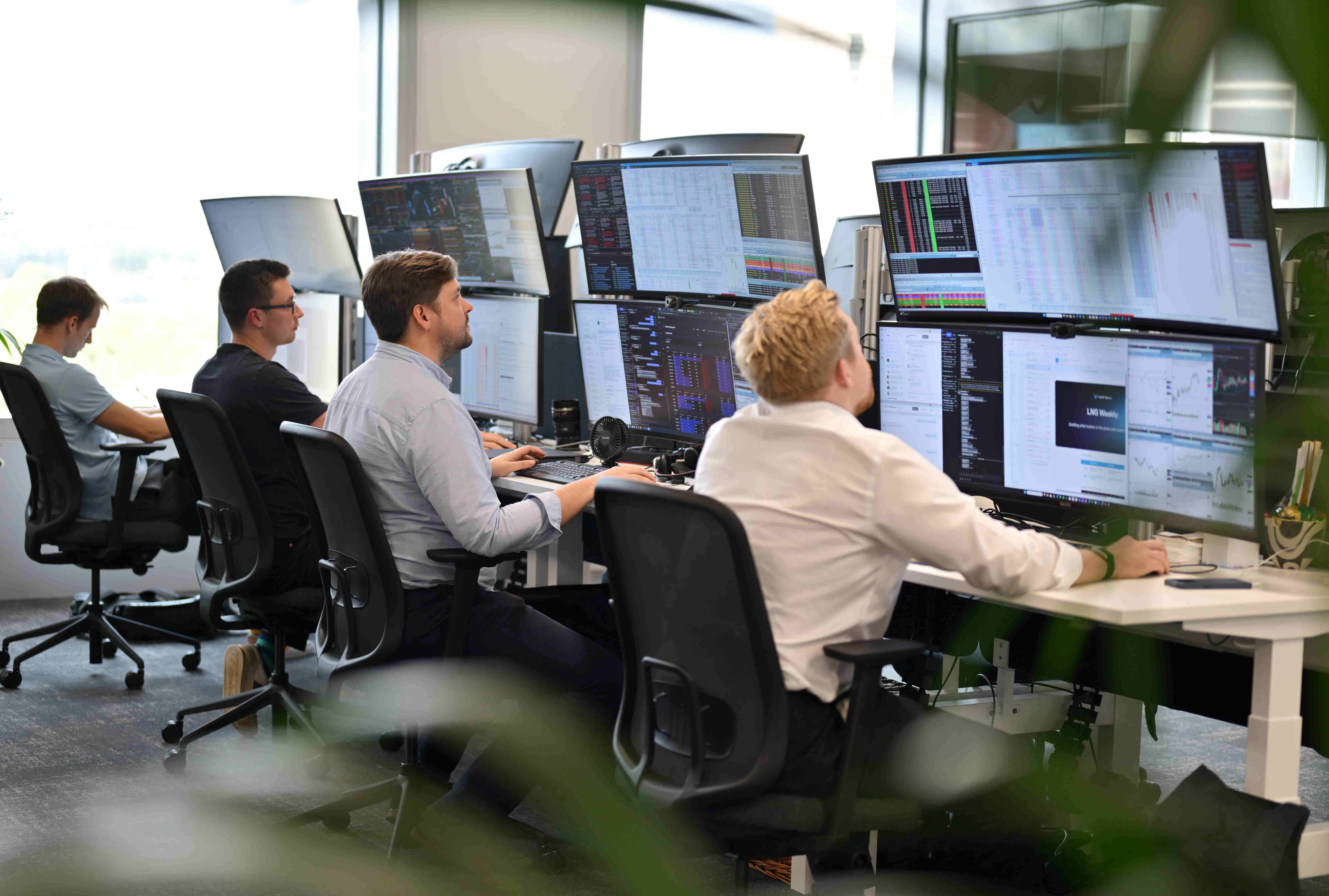 A row of people sit at desks looking at screens showing energy data.