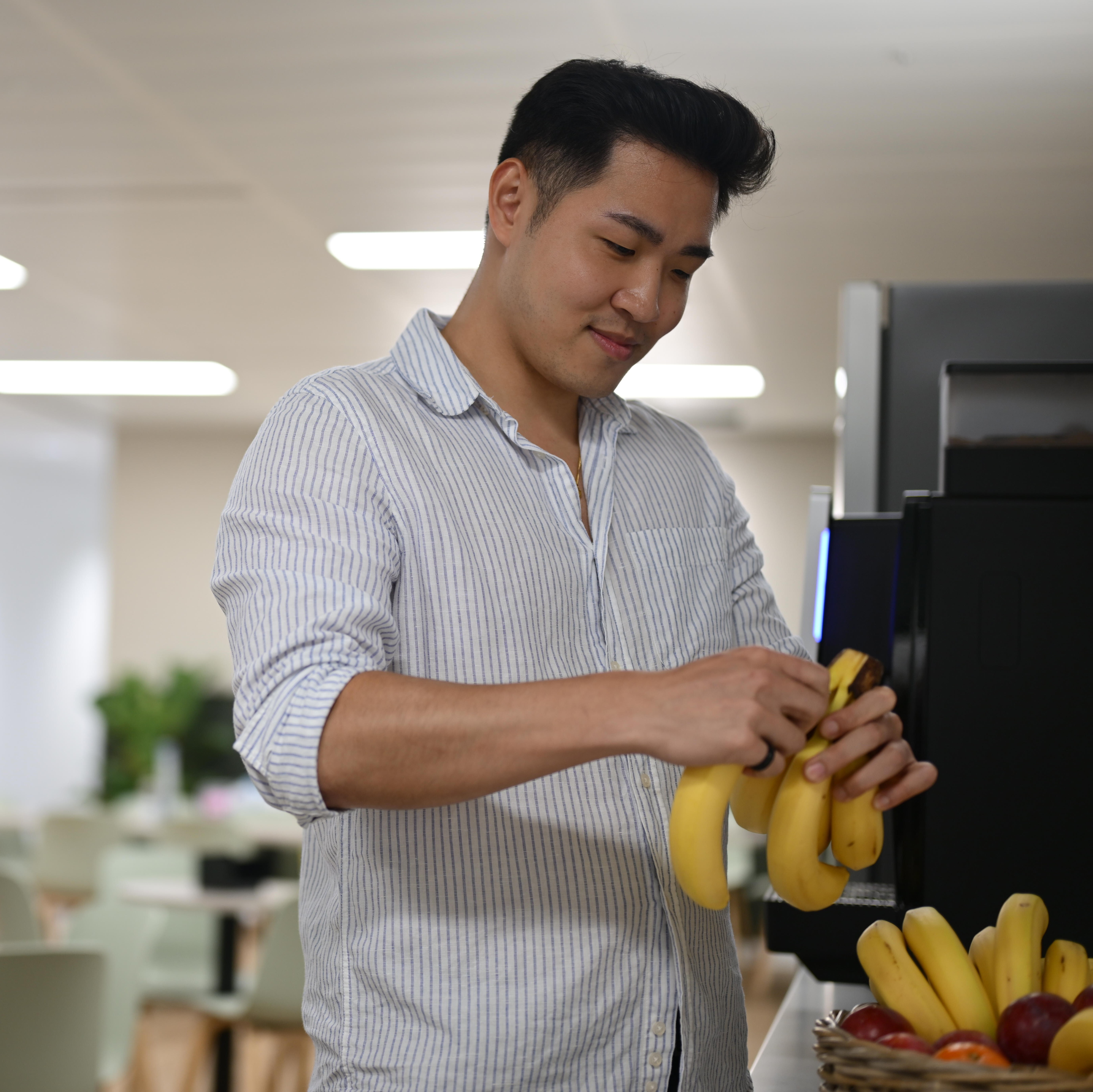 A person picks a banana from an overflowing fruit bowl