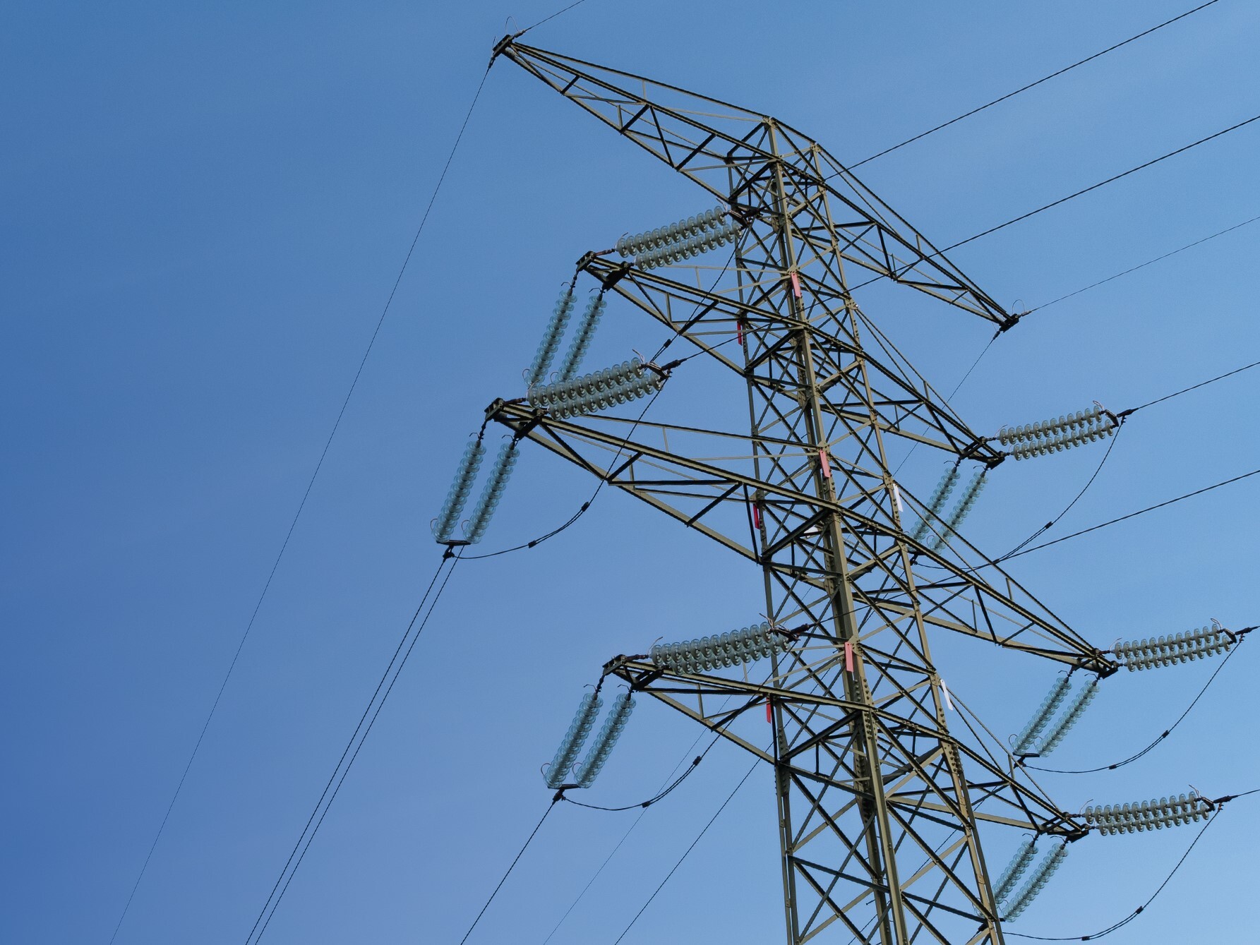 A view from below of an electricity pylon set against a clear blue sky.