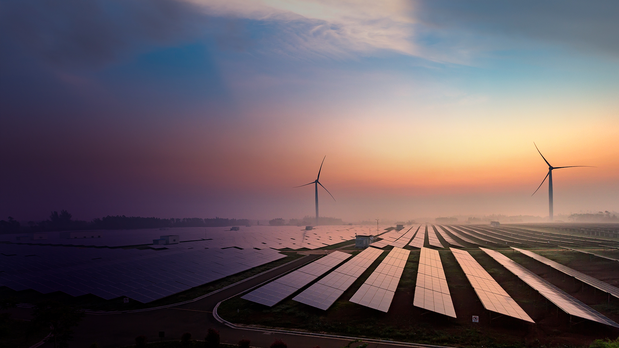 A field of solar panels set against a glowing sunset.
