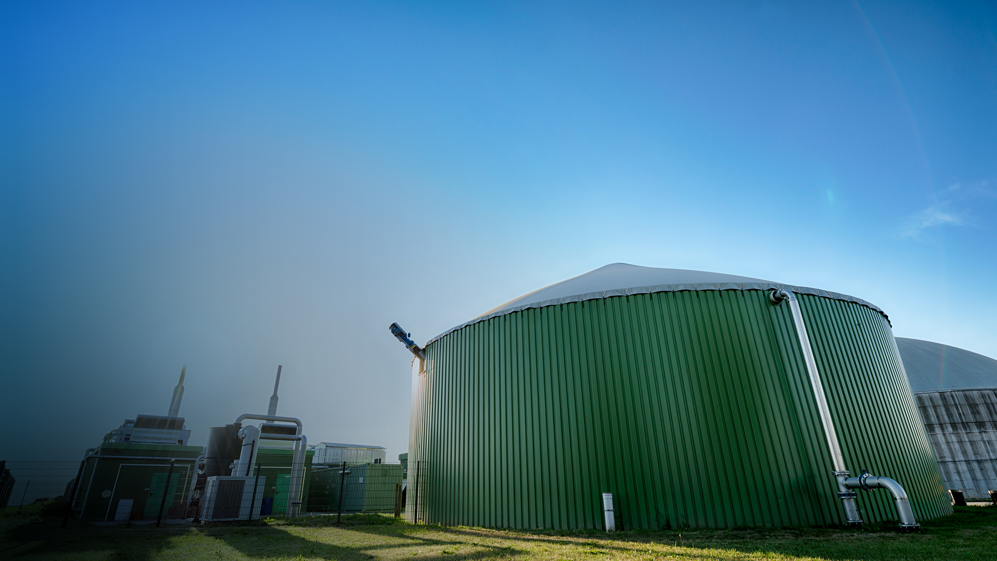 A green anaerobic digester framed by a clear blue sky.