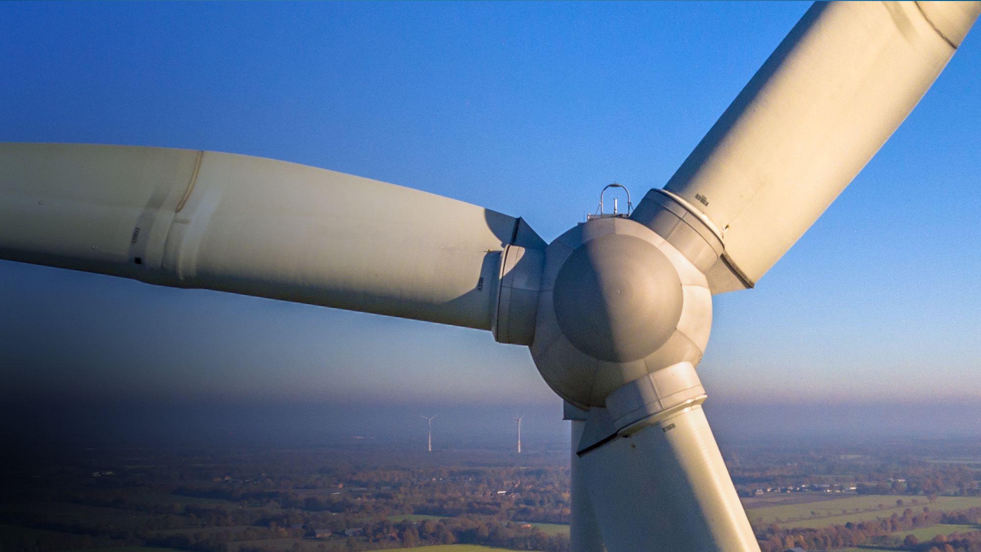 A close up of a wind turbine backed by fields and blue sky.