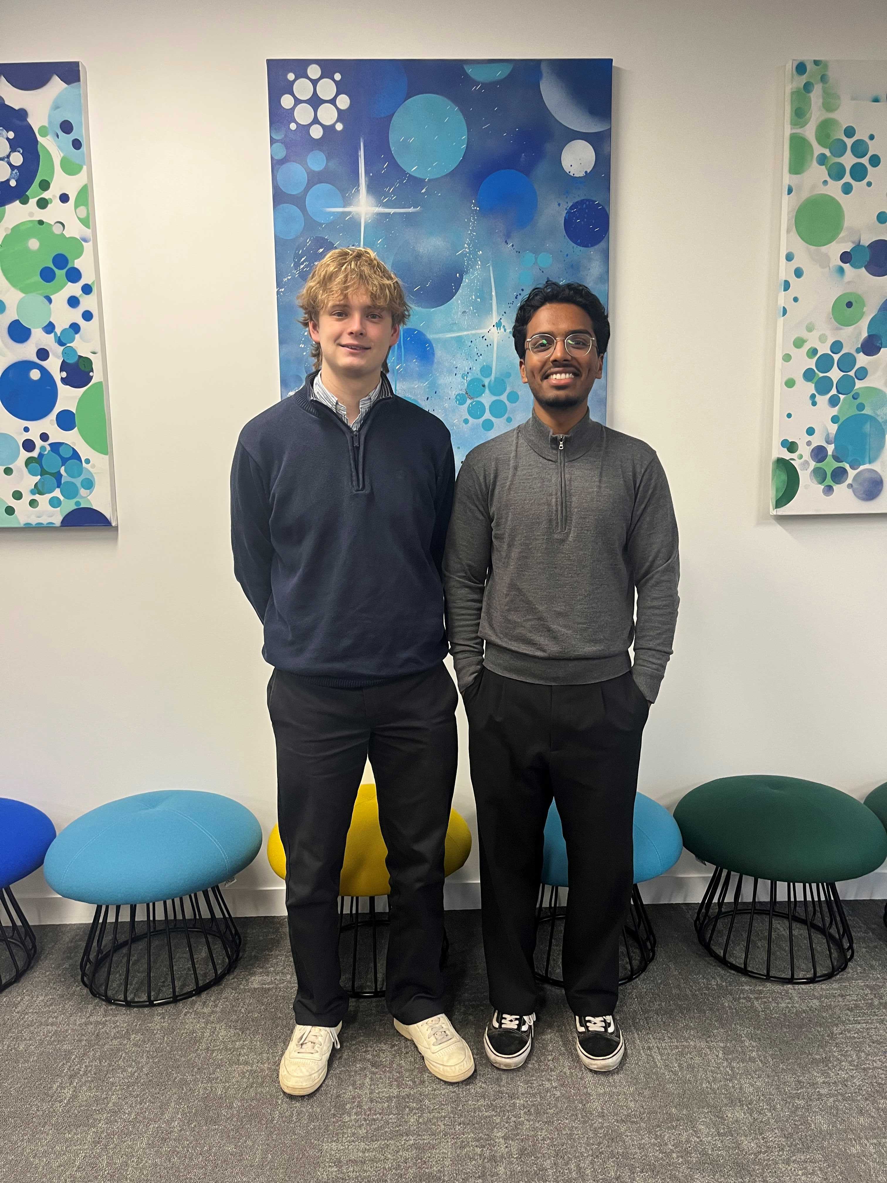 Two people stand together against a wall with blue and green artwork.