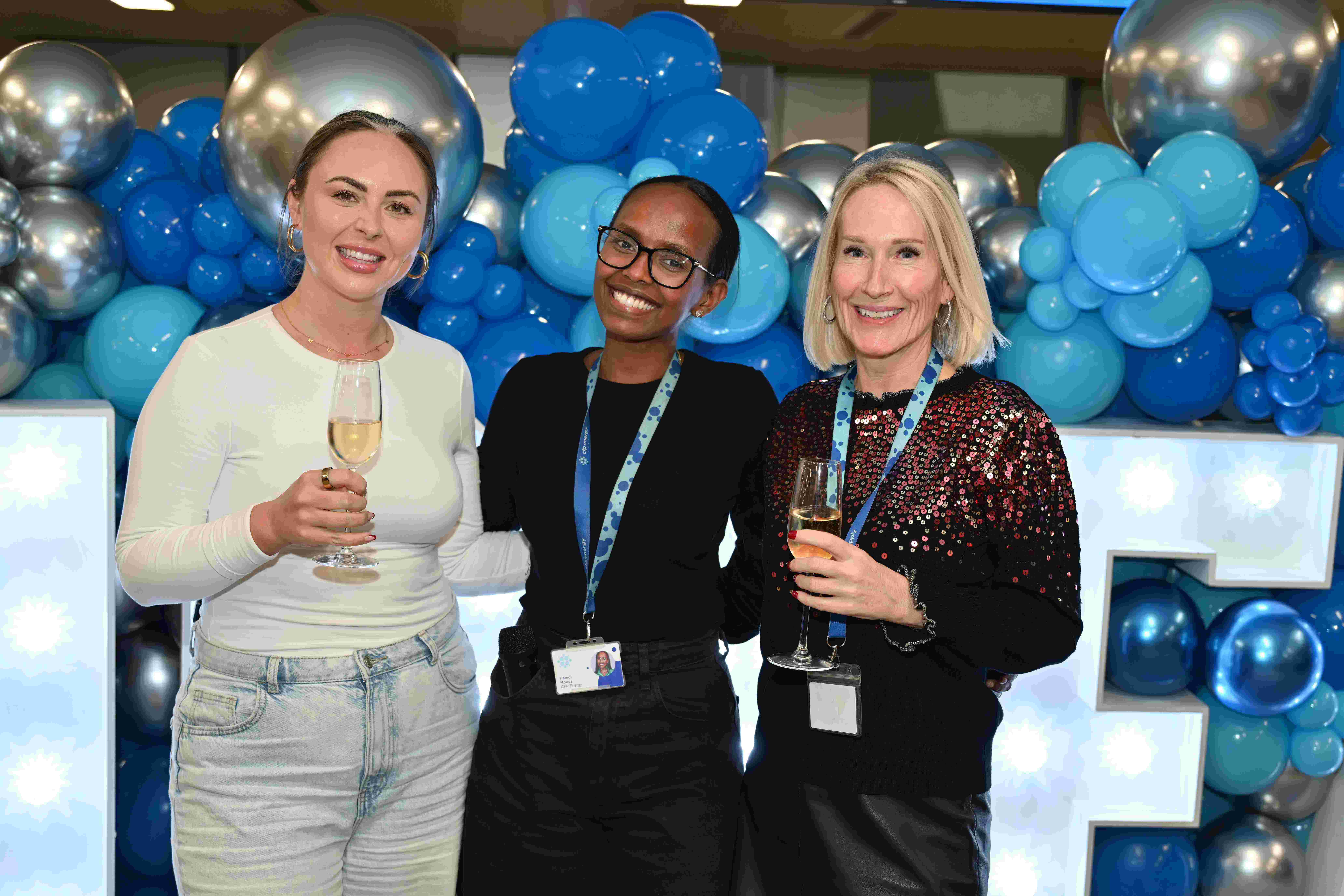 Three people smile in front of balloons and lights