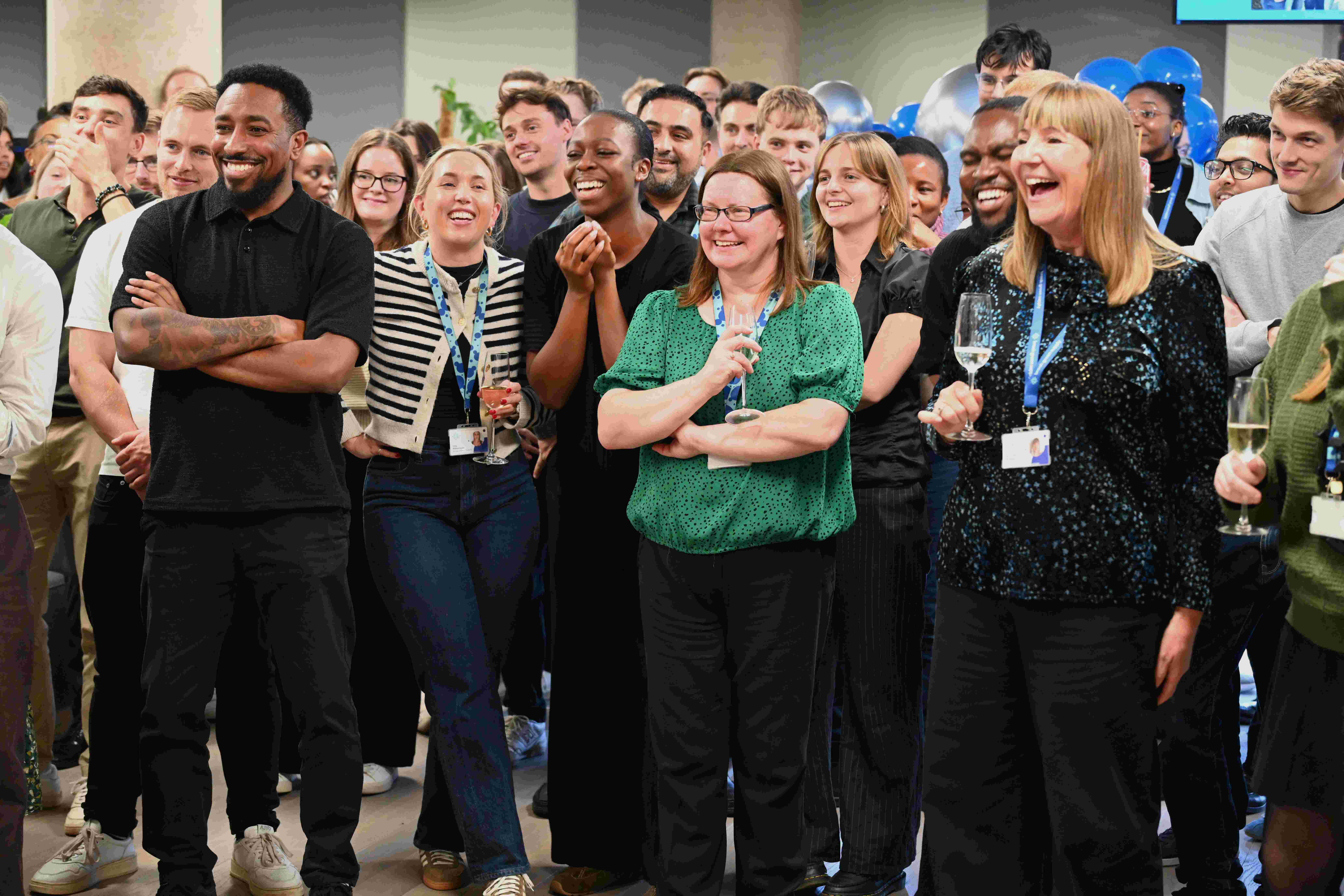A group of people smile and laugh whilst watching something