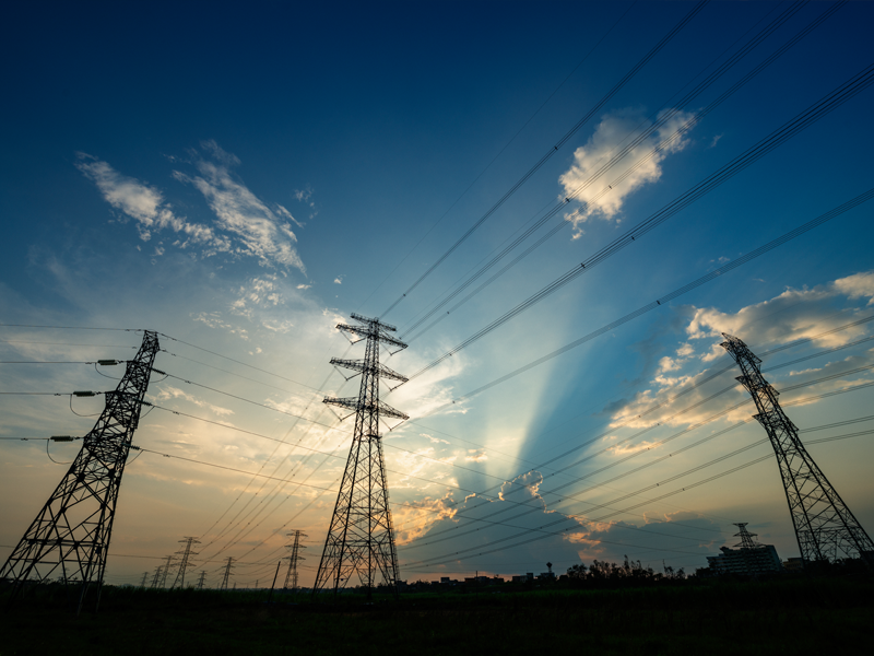 A view from below of some electricity pylons against a blue sky with some light cloud.