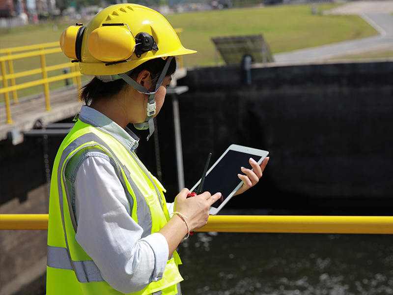 A person in high vis with a yellow hard hat holding a tablet looks down on to a waste pit.