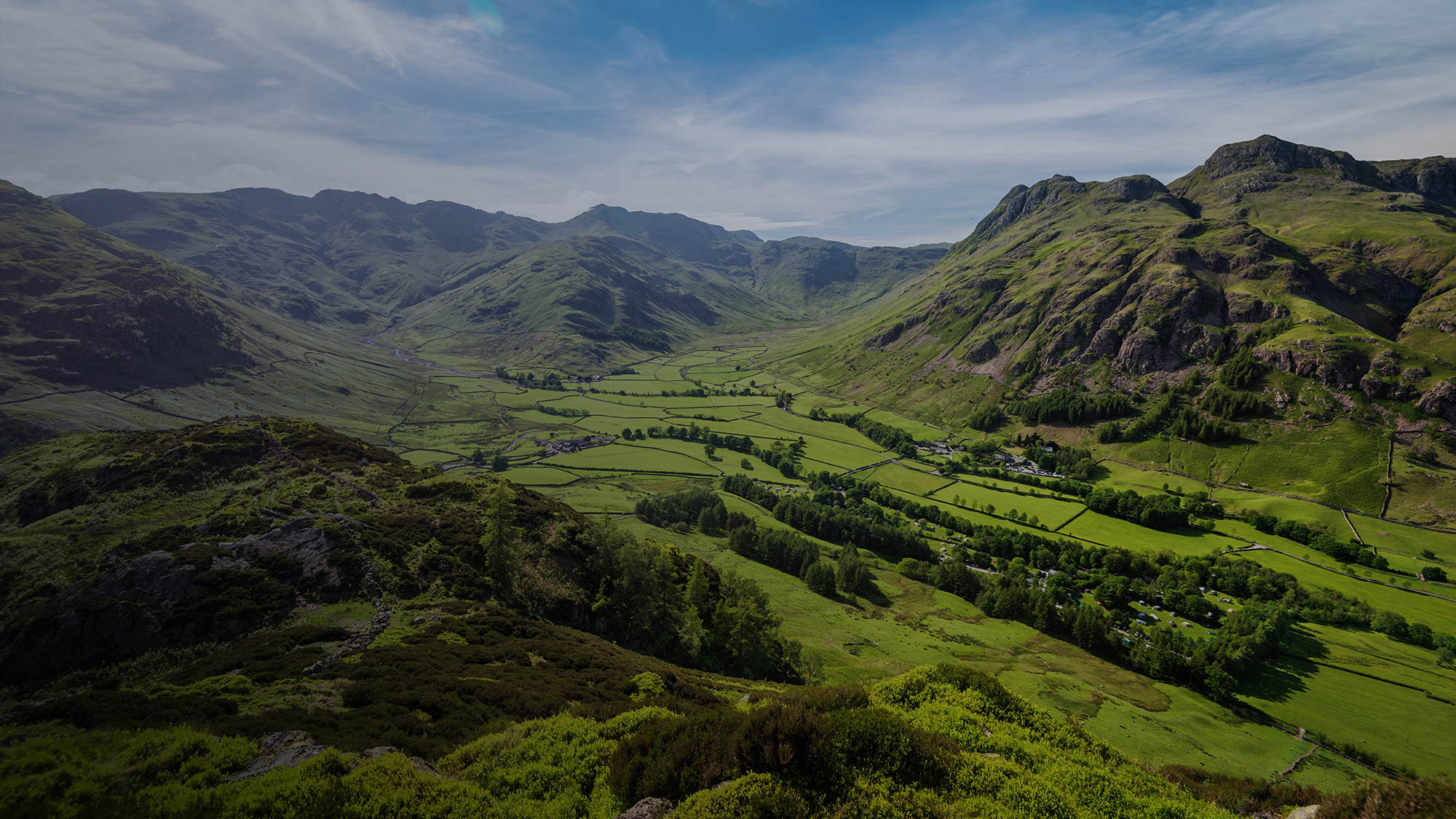 A wide view of a green valley surrounded by tall, rugged hills under a blue sky with light clouds.