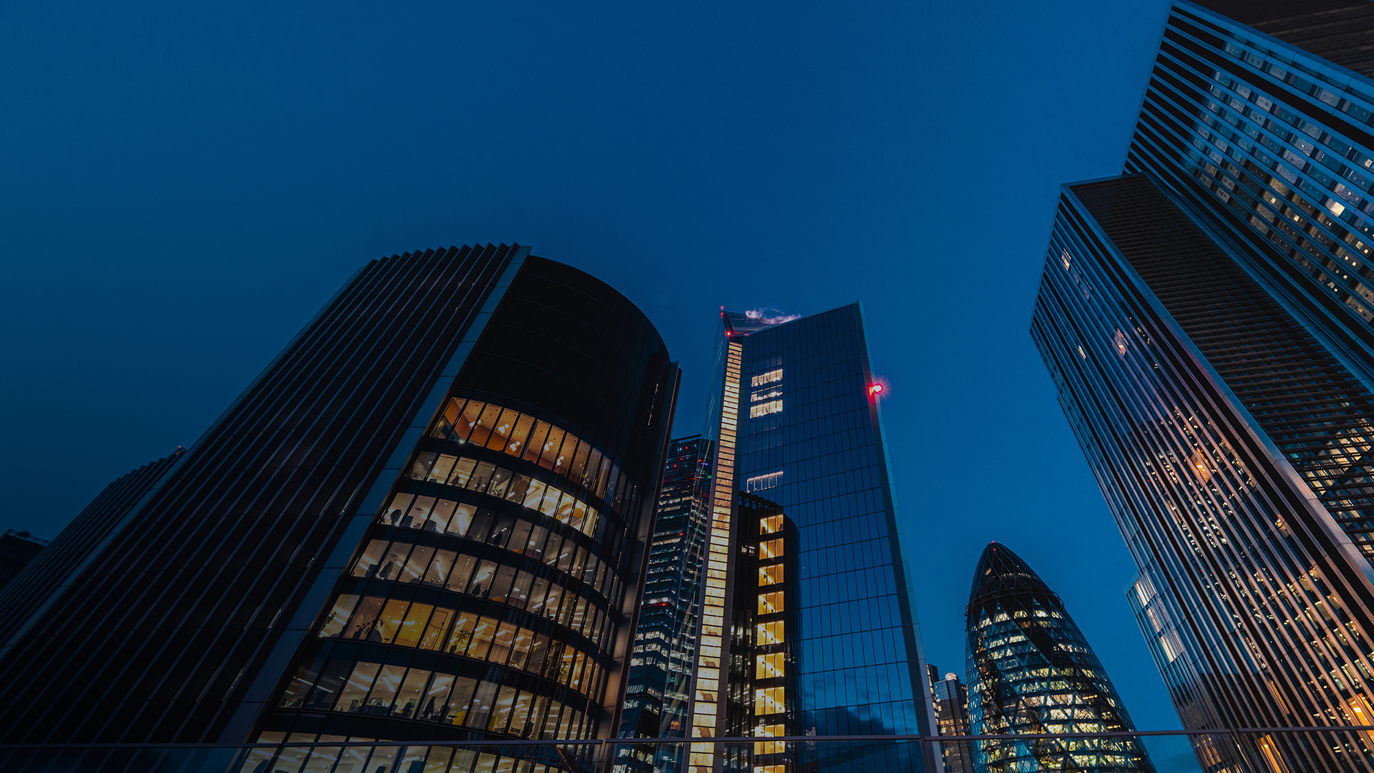 A view from below of some towering buildings against a dark blue sky.