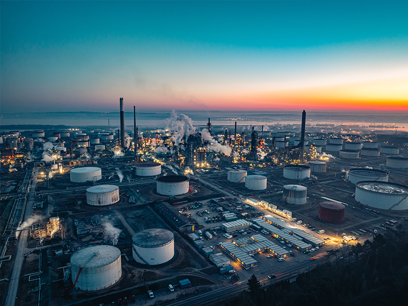 A large industrial processing facility at dusk, lit up against a blue and orange sky.