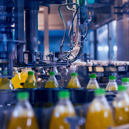 A long row of orange drinks in bottles with green lids move through a factory production line.