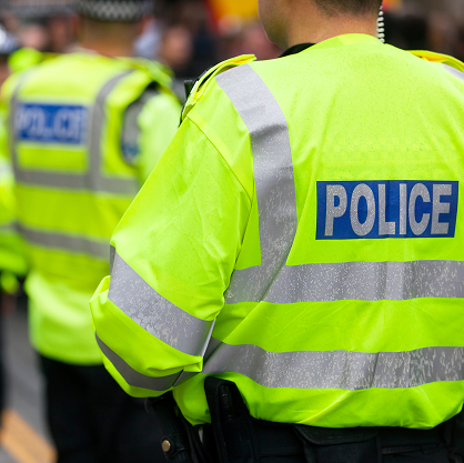 A behind view of several police officers wearing LED jackets with police emblazoned on the back in blue.