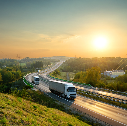 Two lorries speed along a motorway while the sun rises in the background.