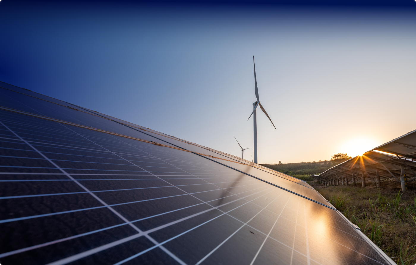 A side view of solar panels in the foreground with two wind turbines in the background against a blue sky.