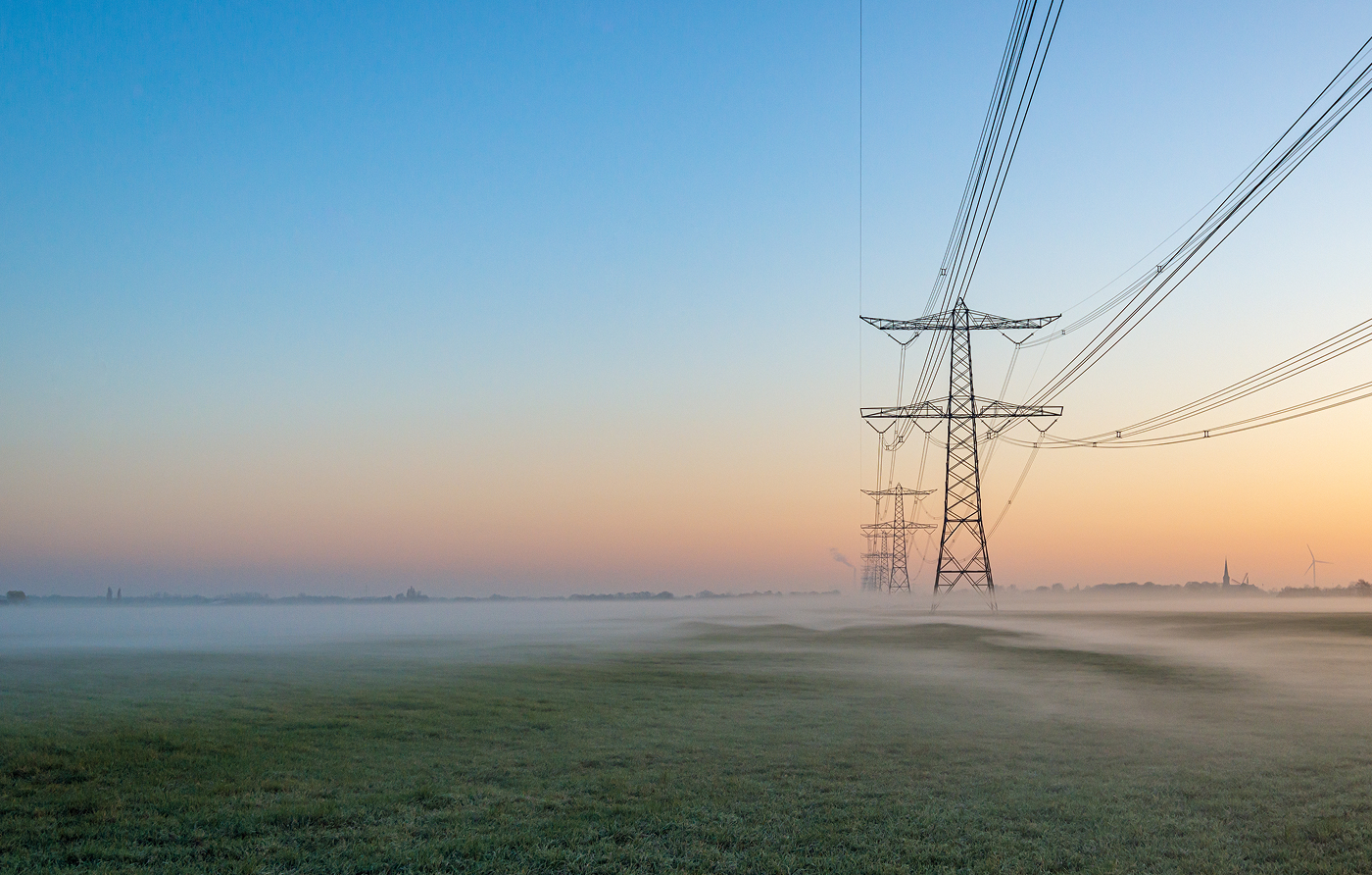 A row of electricity pylons against a dawn sky, surrounded by low-lying mist.