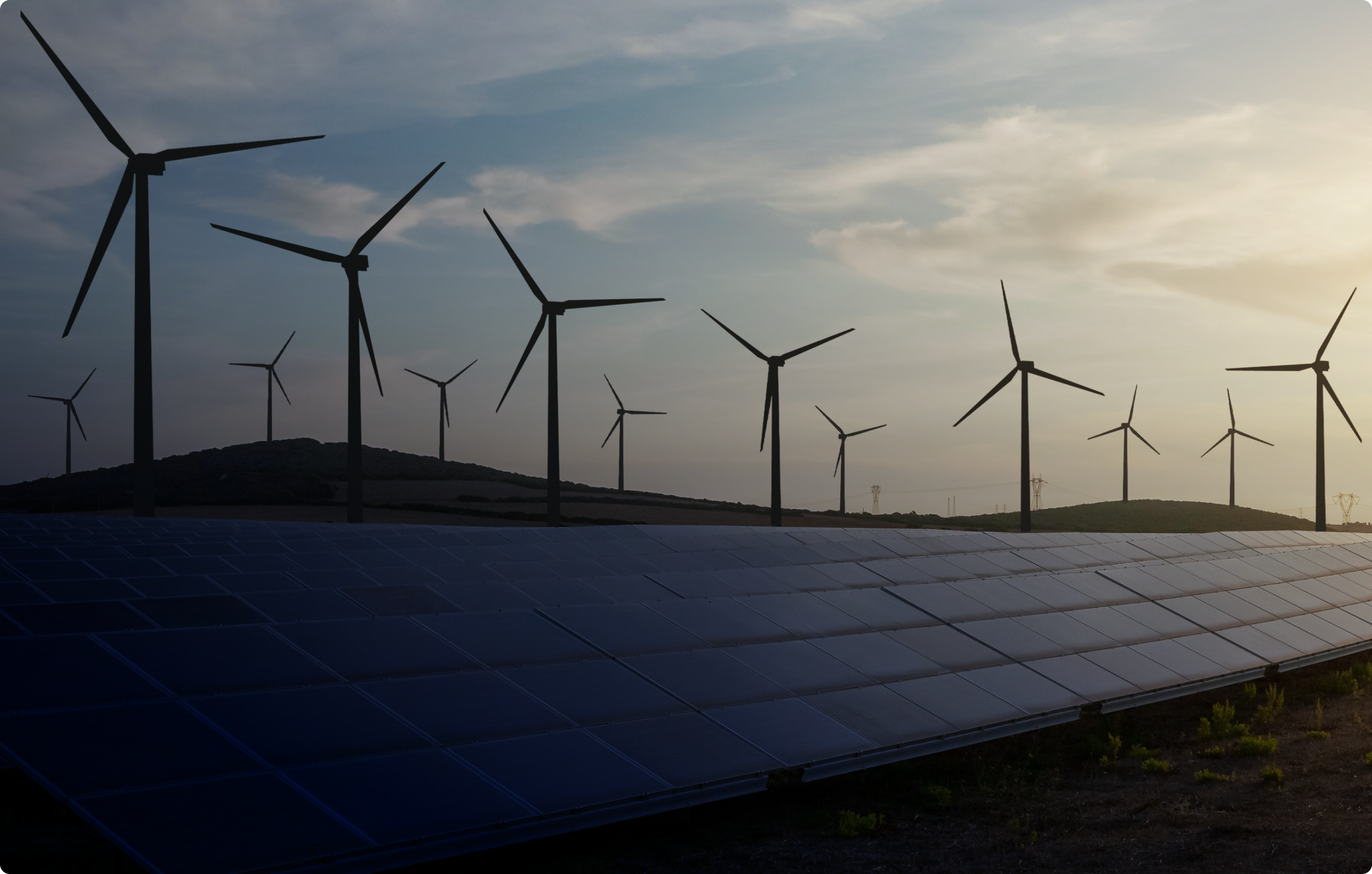 A row of wind turbines against a skyline with solar panels in the foreground.